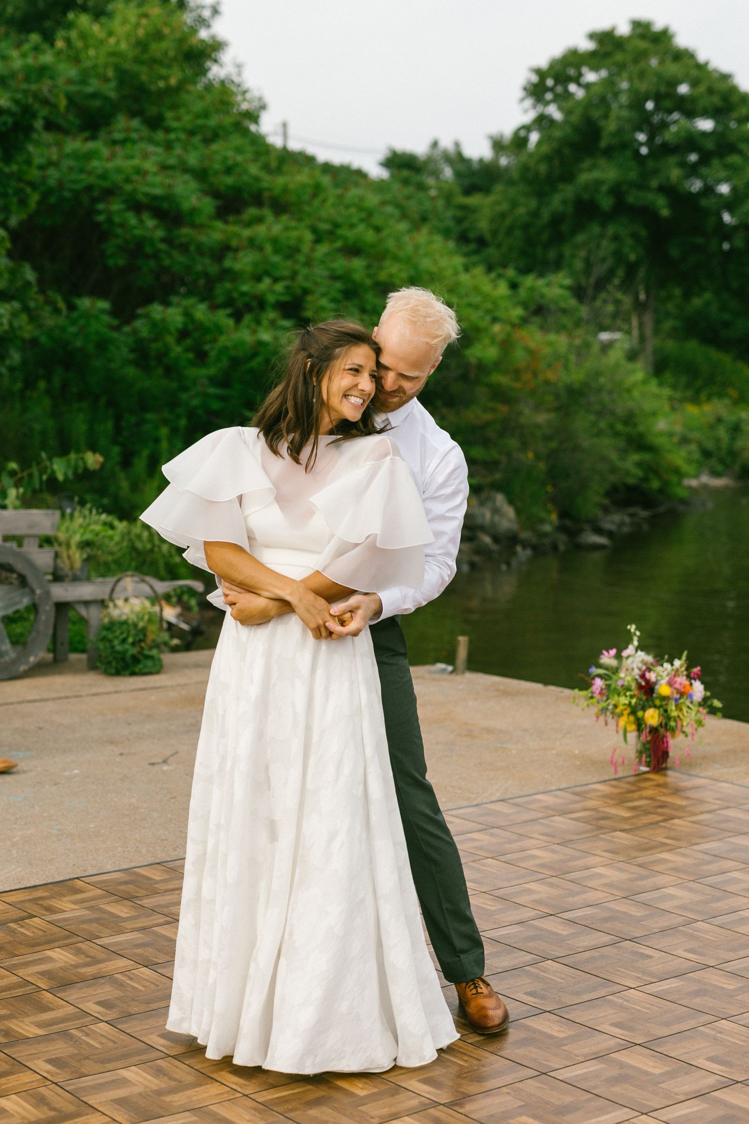 A joyful wedding couple embraces and laughs together in front of a red barn on their special day.