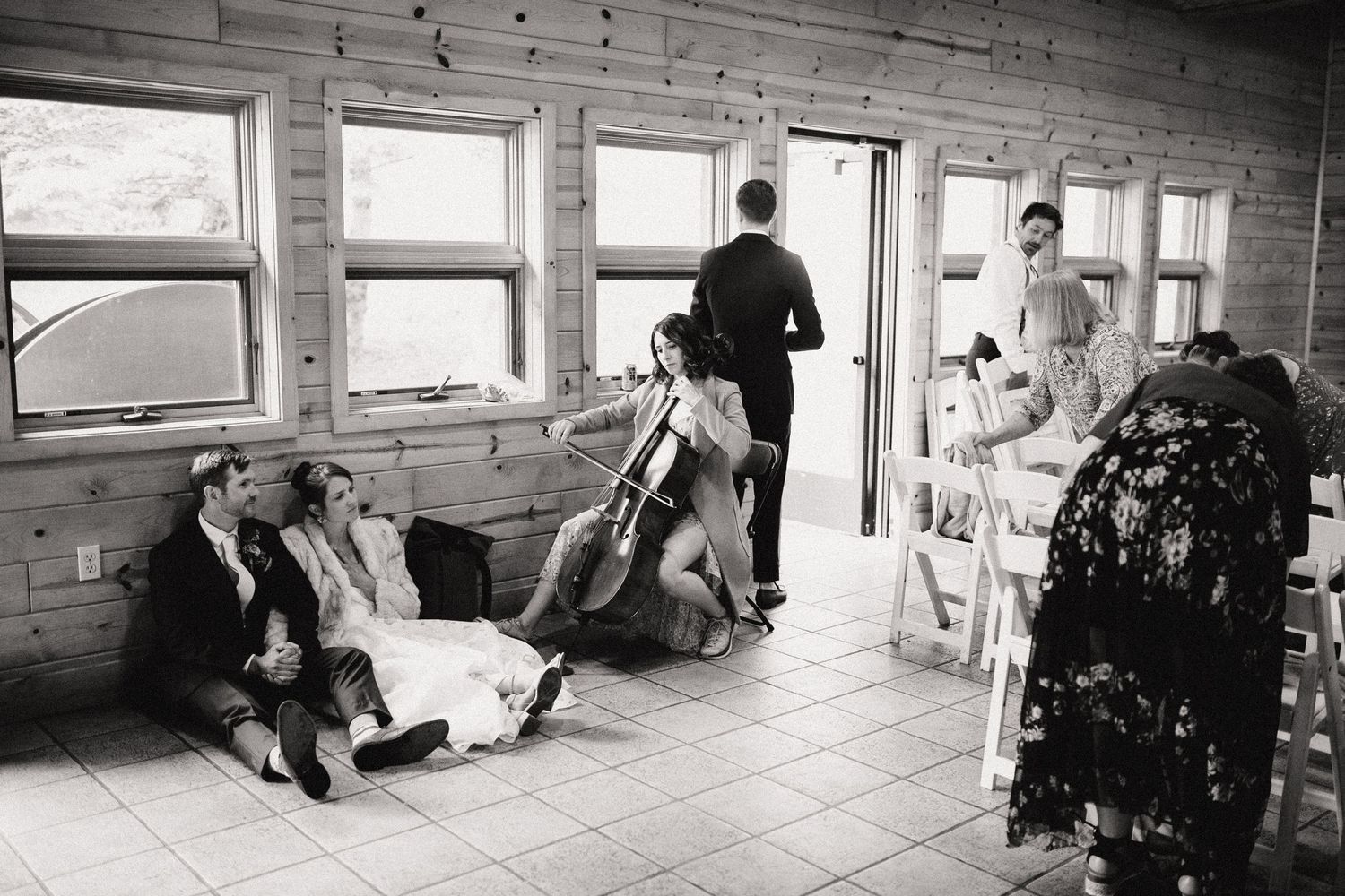 A candid black and white photo showing people relaxing in a casual indoor sunlit setting with multiple windows.
