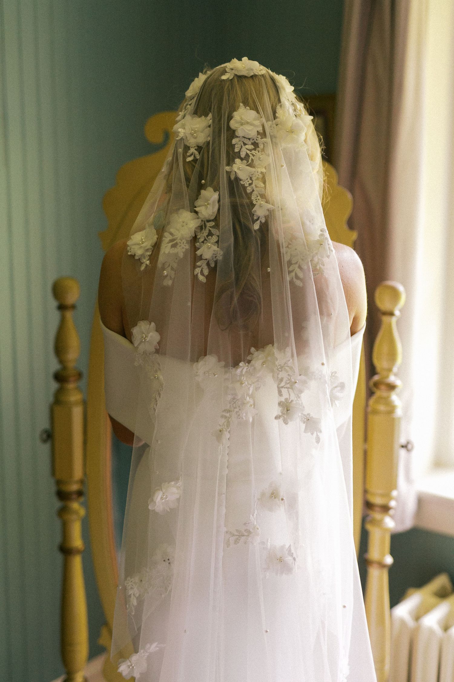 White wedding veil with delicate lace details hanging against a soft green wall.