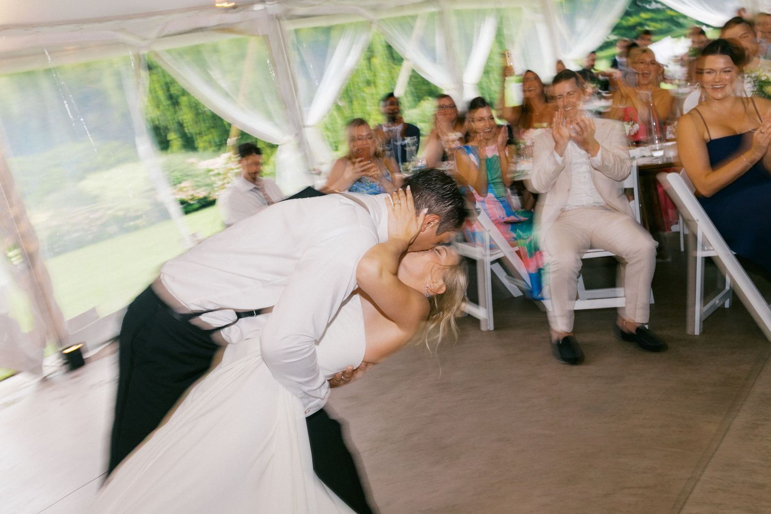 A couple performs a dramatic dance dip during a wedding reception under a white tent with guests watching.