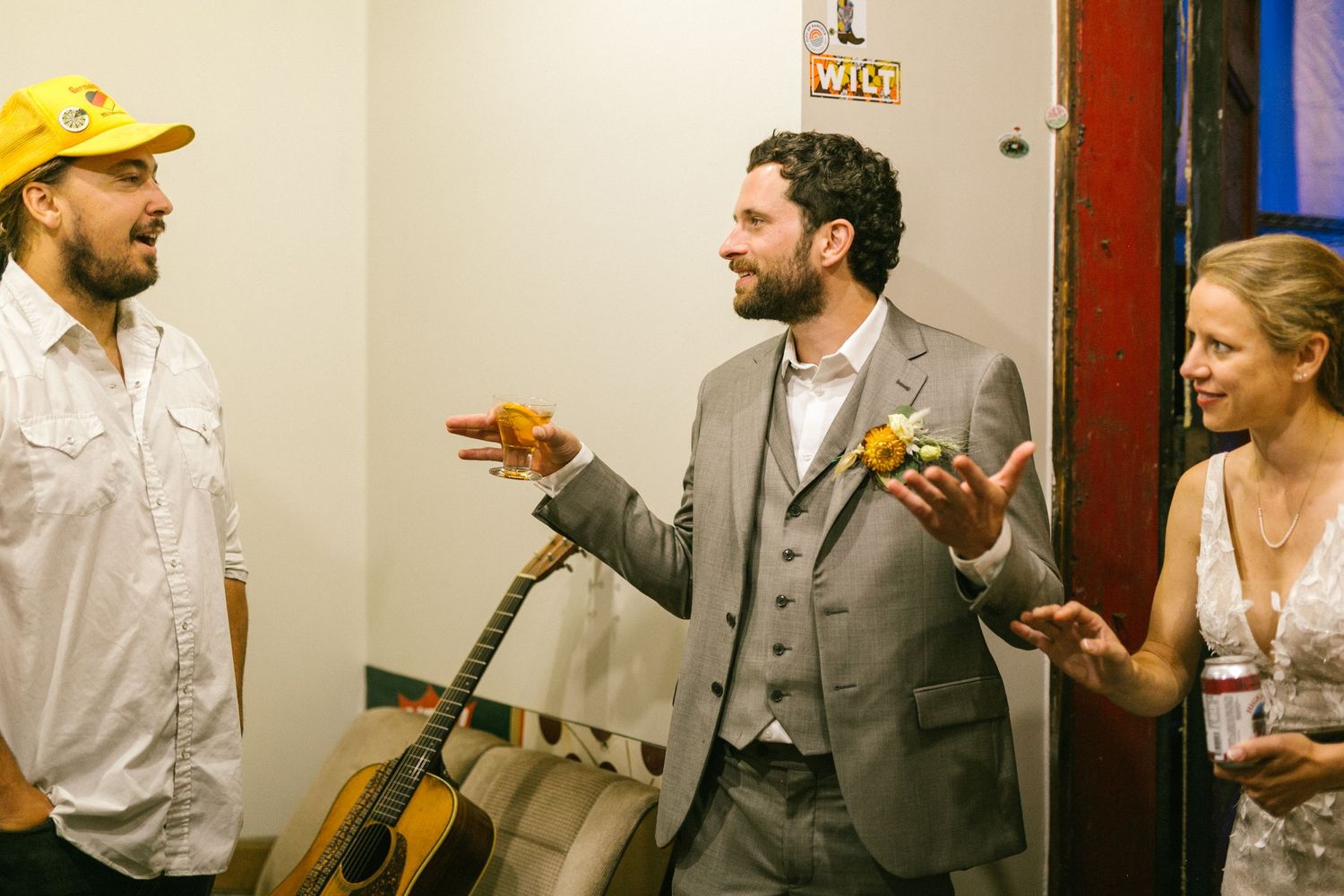 Three wedding guests share a laugh while enjoying drinks and appetizers at a celebratory event.