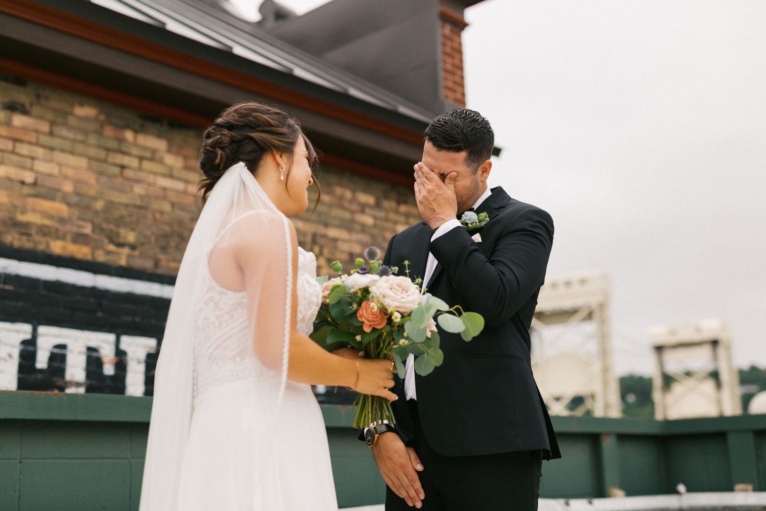 Emotional groom covering his mouth in tears during a first look moment with his bride outdoors.