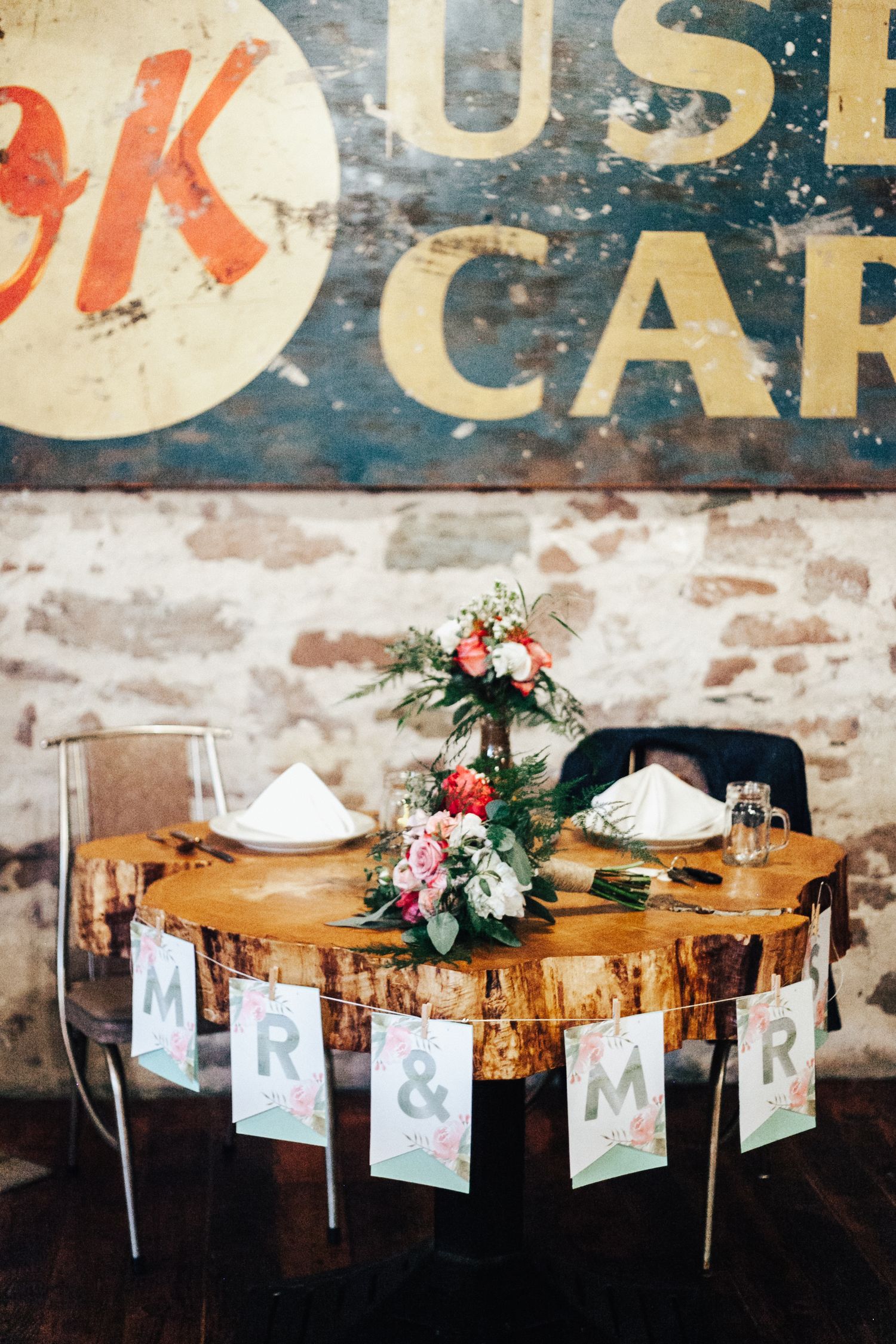 A rustic wooden table decorated with floral arrangements and letter banners for a wedding reception.