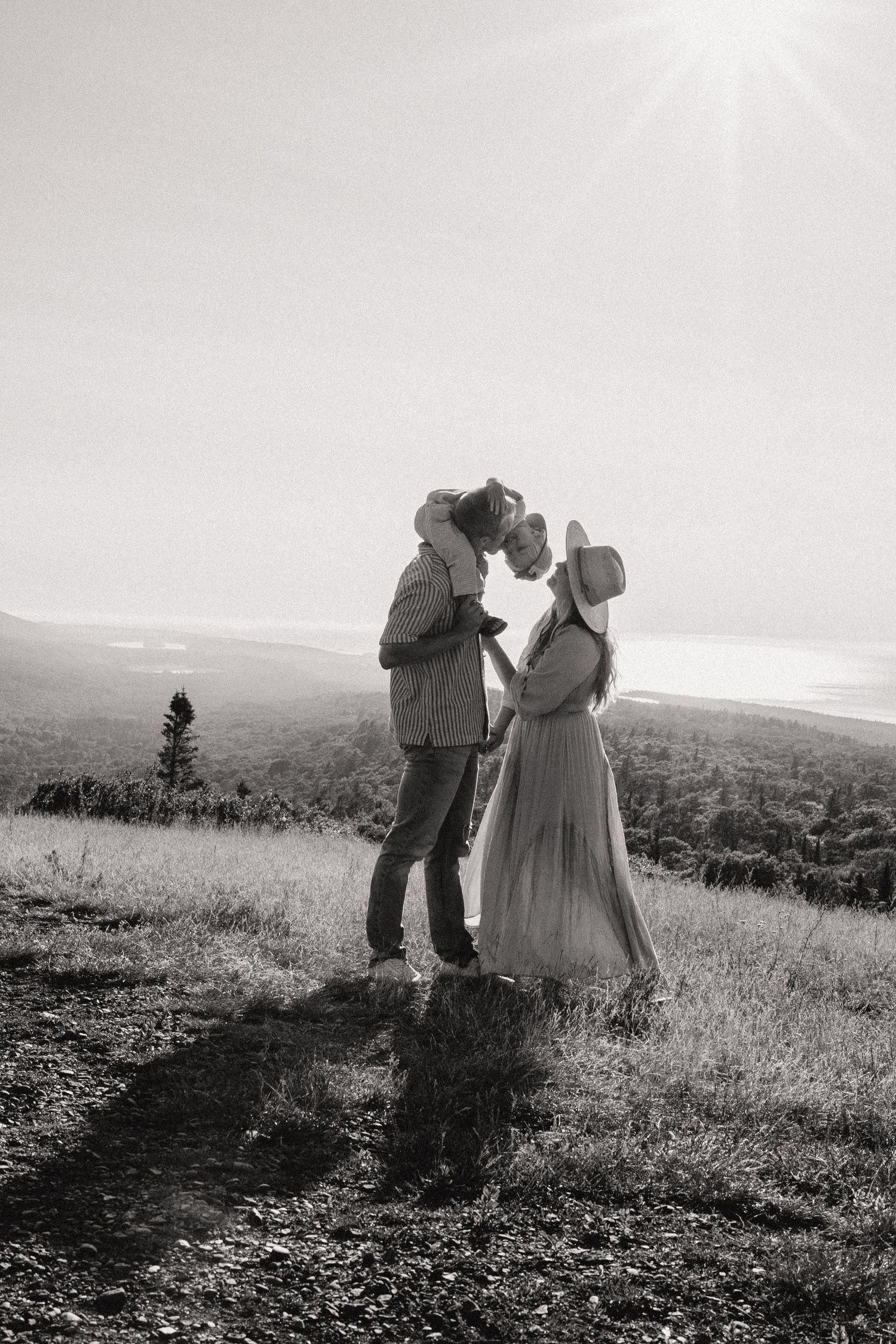 Black and white photo of a couple kissing on a hilltop with a scenic landscape behind them.