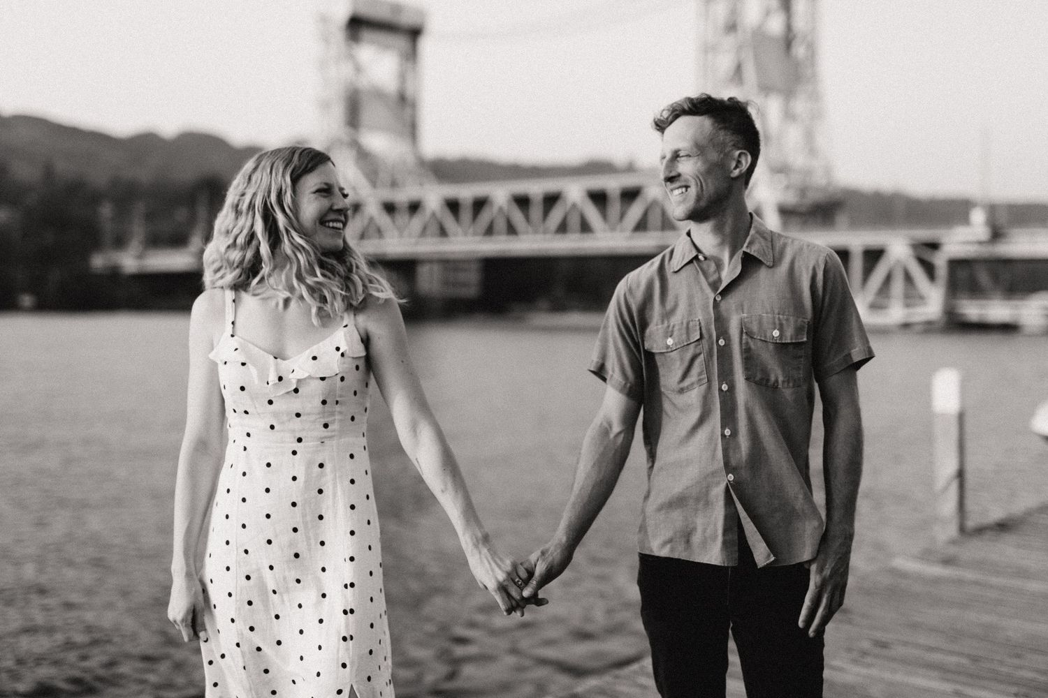 Couple holding hands while standing near a bridge during golden hour.