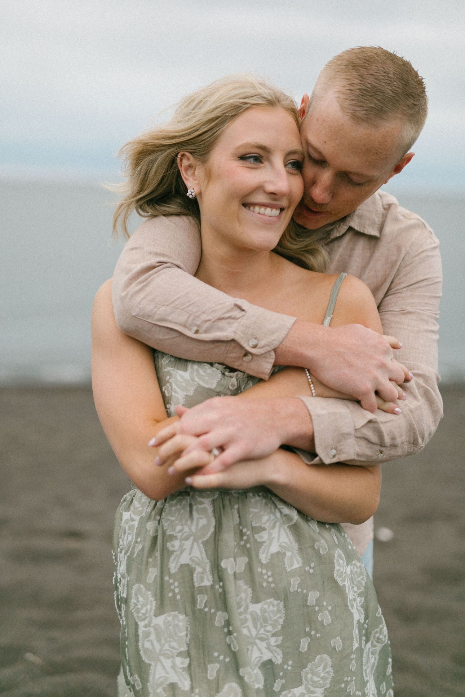 Couple shares tender moment on beach with ocean and cloudy sky in background.