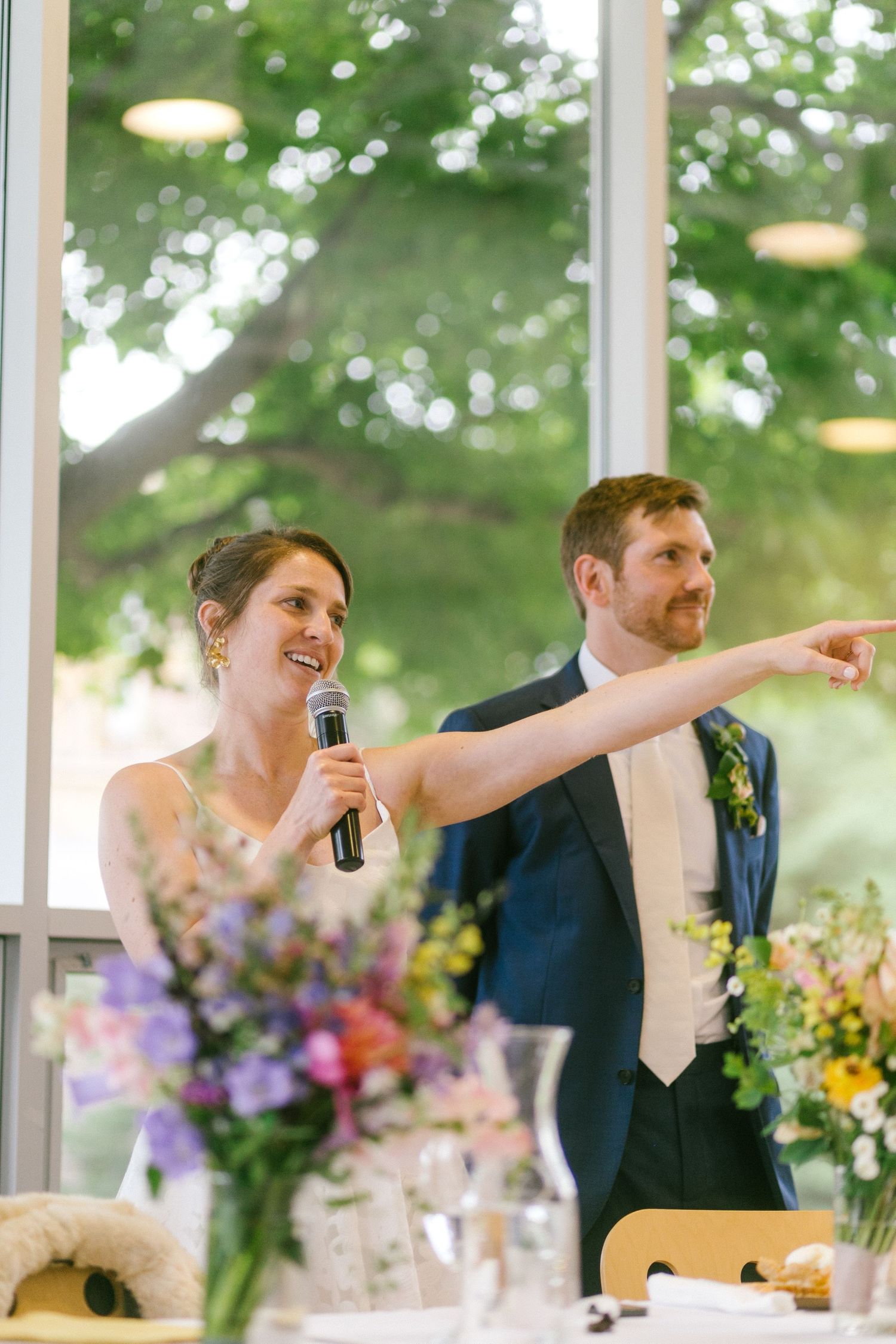 A couple sharing a joyful moment while giving speeches at their reception with floral centerpieces.
