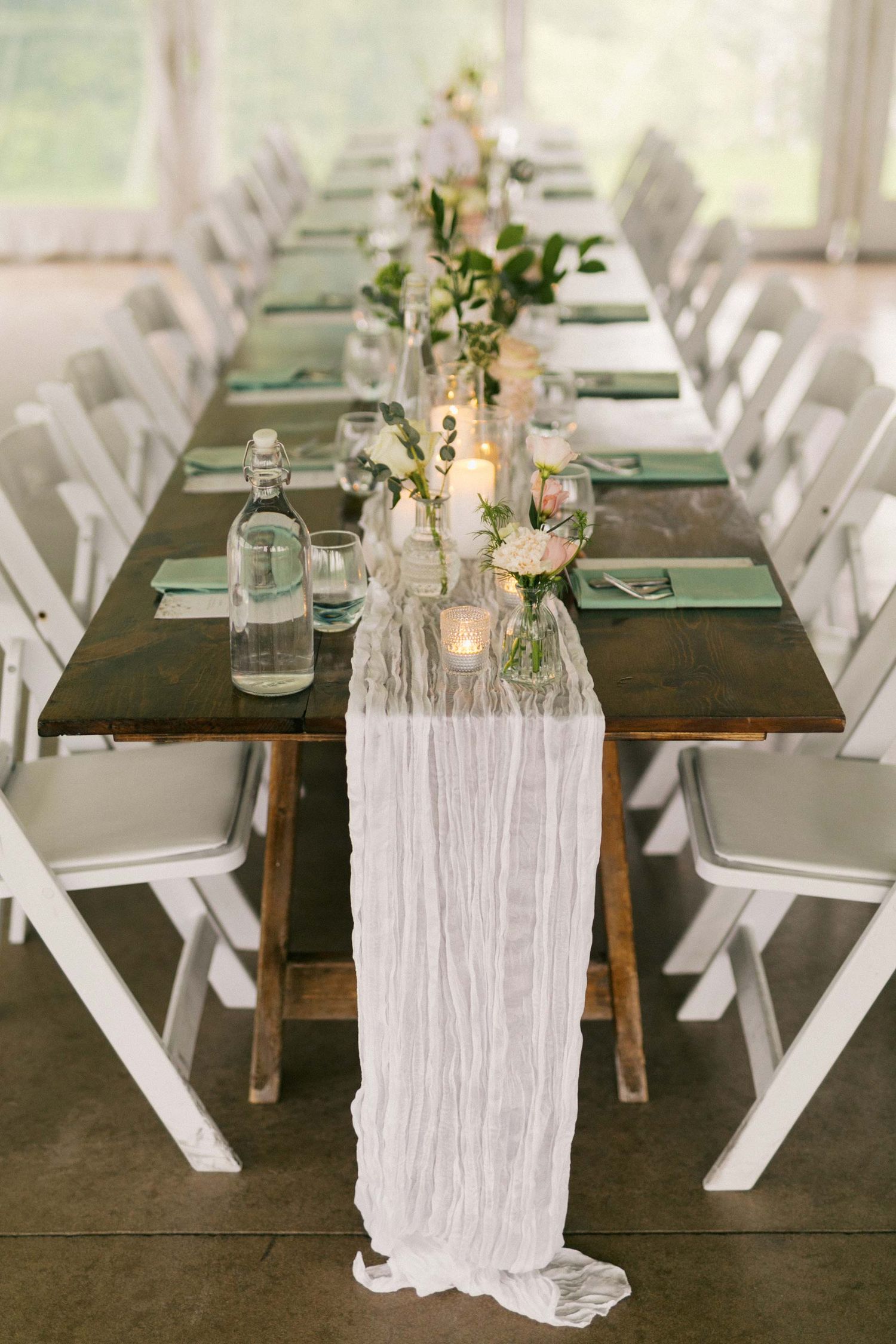 Elegant wedding reception table settings with white chairs, dark wood tables, and flowing white fabric table runners.