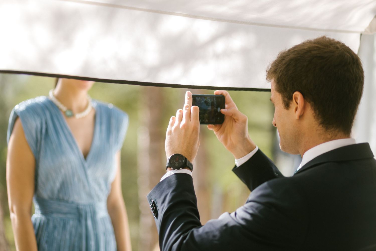 Wedding guest takes a photo of someone wearing a light blue dress in a soft-lit setting.