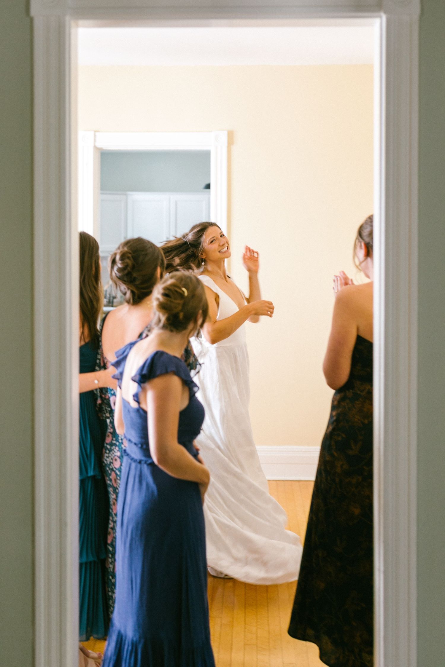 A group of people in formal attire gather in a bright room with white walls and hardwood floors.