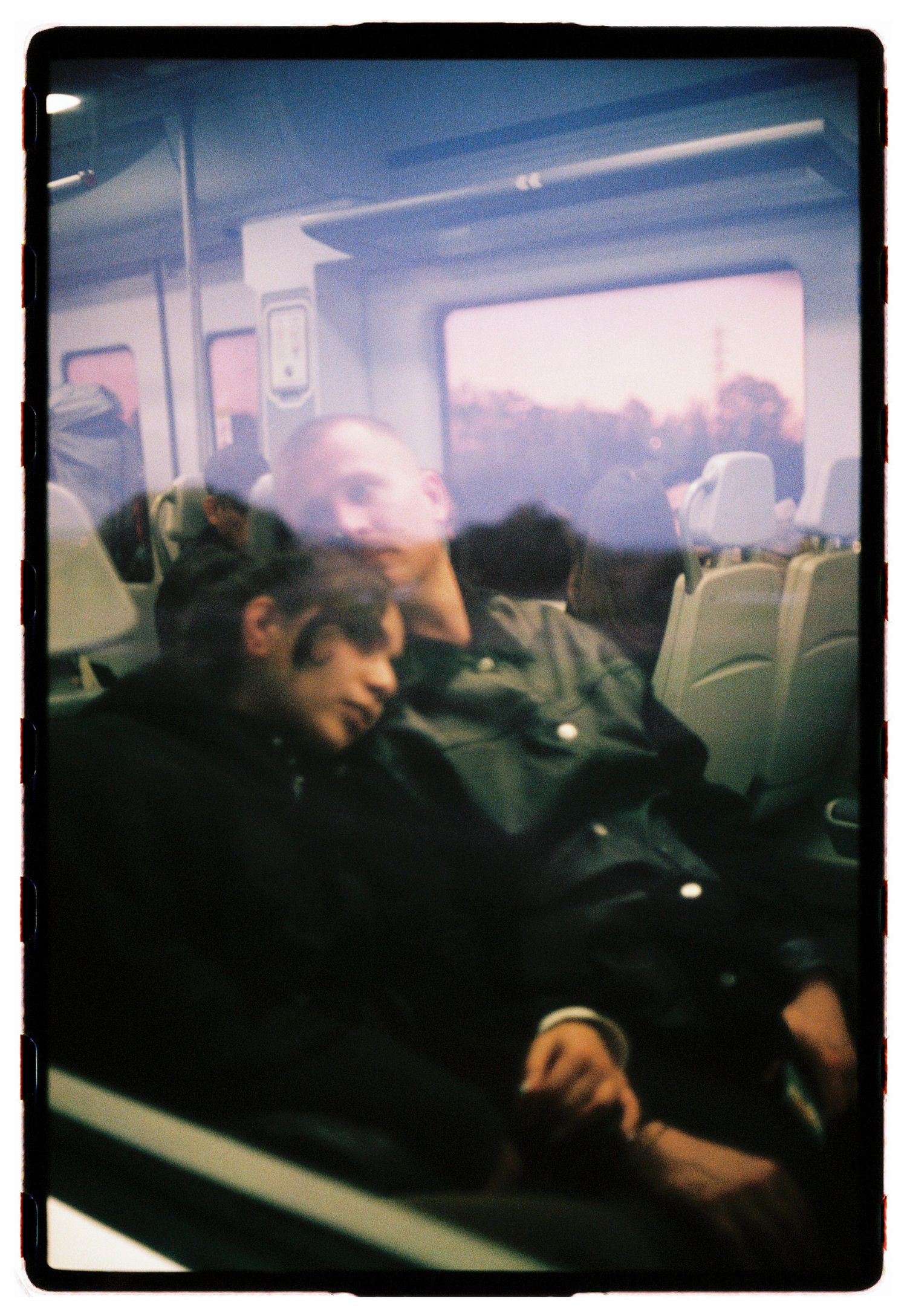 Two passengers resting and sleeping in seats on a train, viewed through a window reflection.