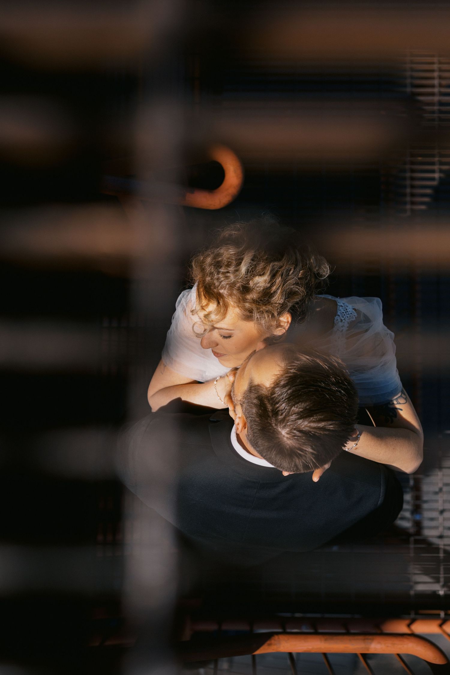 Couple sharing a romantic kiss, viewed through wooden slats in warm golden light.