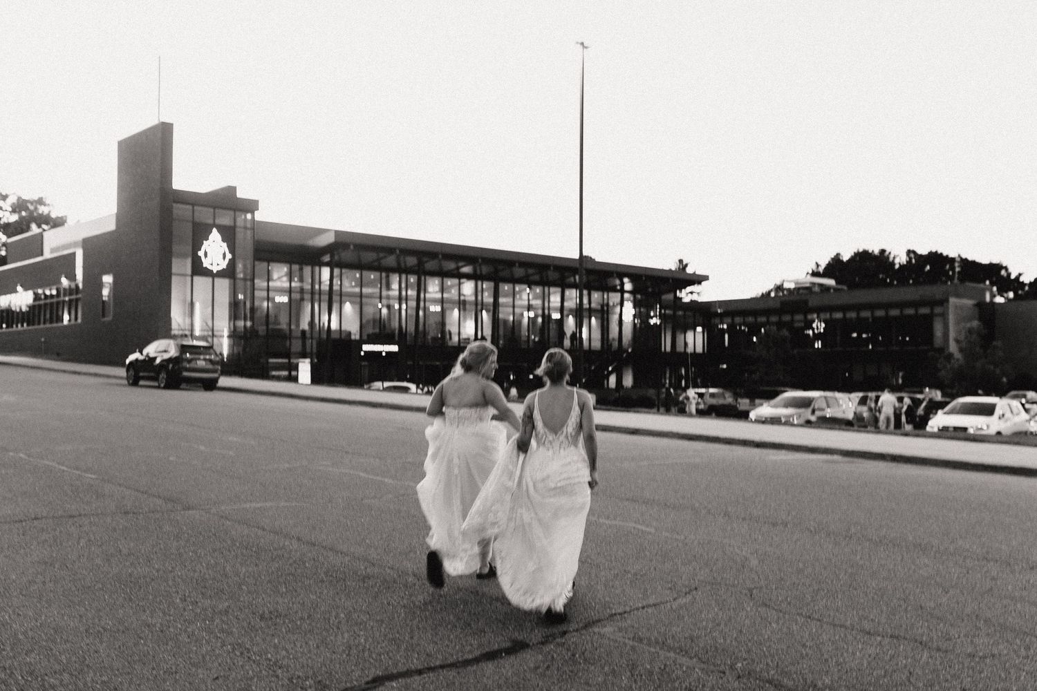 A bride in a flowing white dress walks through a field while holding her gown on a sunny wedding day.