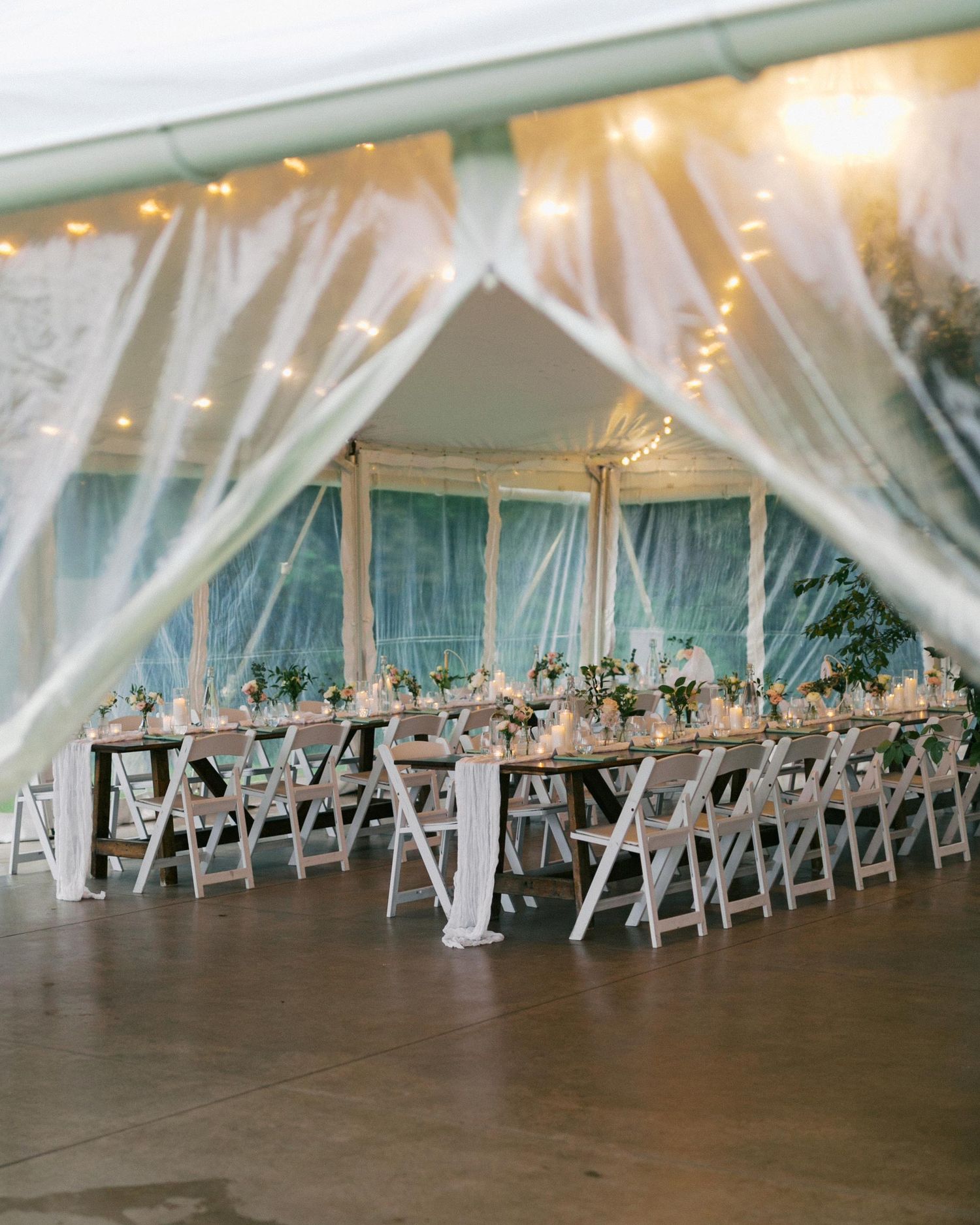 Elegant wedding reception setup with white drapes, string lights and long tables in an airy tent venue.