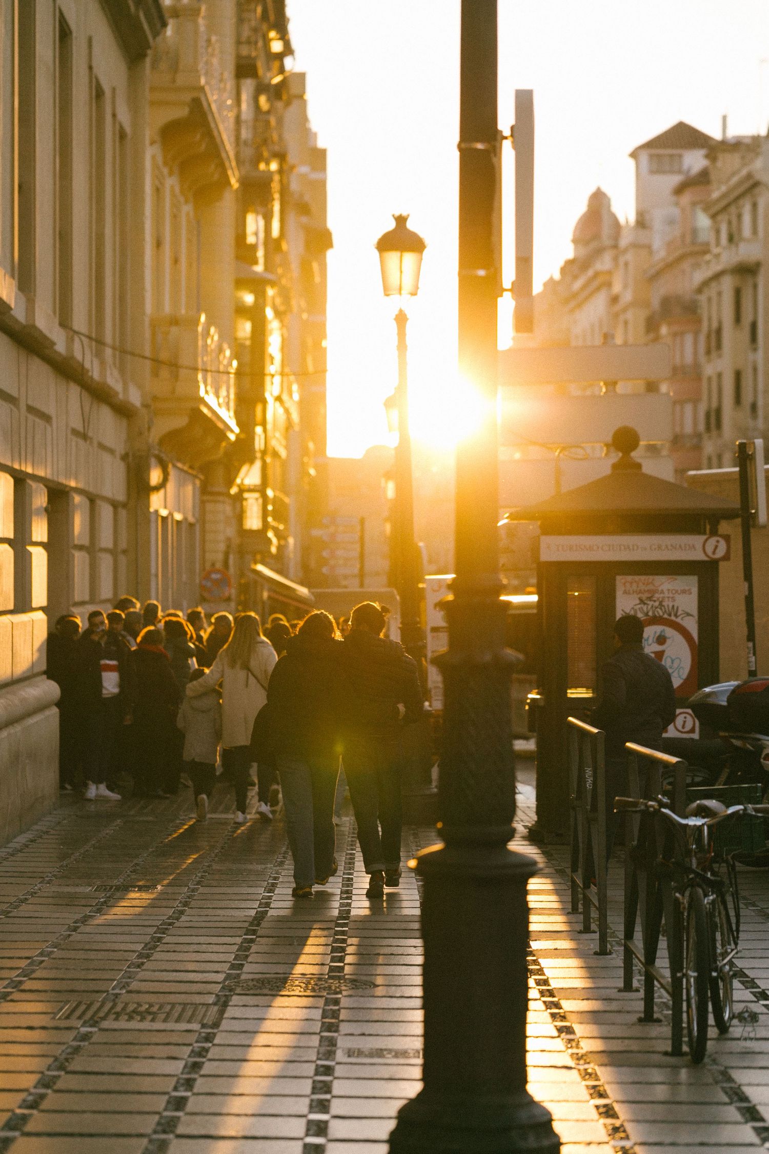 Golden sunlight illuminates a bustling European street with historic architecture and lampposts.