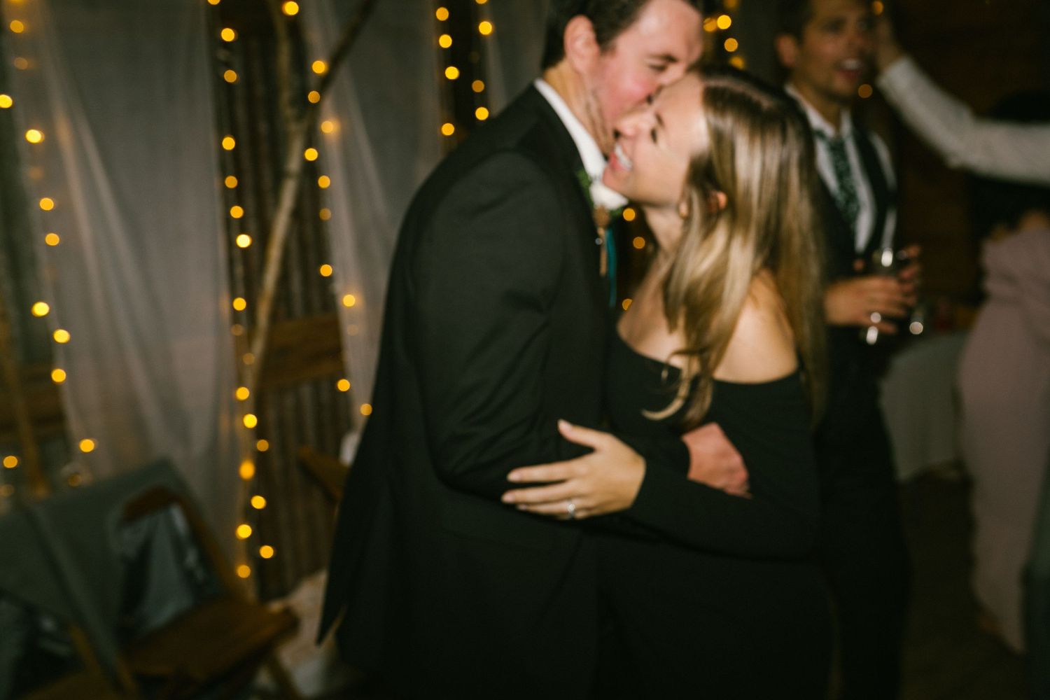 Couple embracing in a passionate kiss during a celebration with string lights in the background.