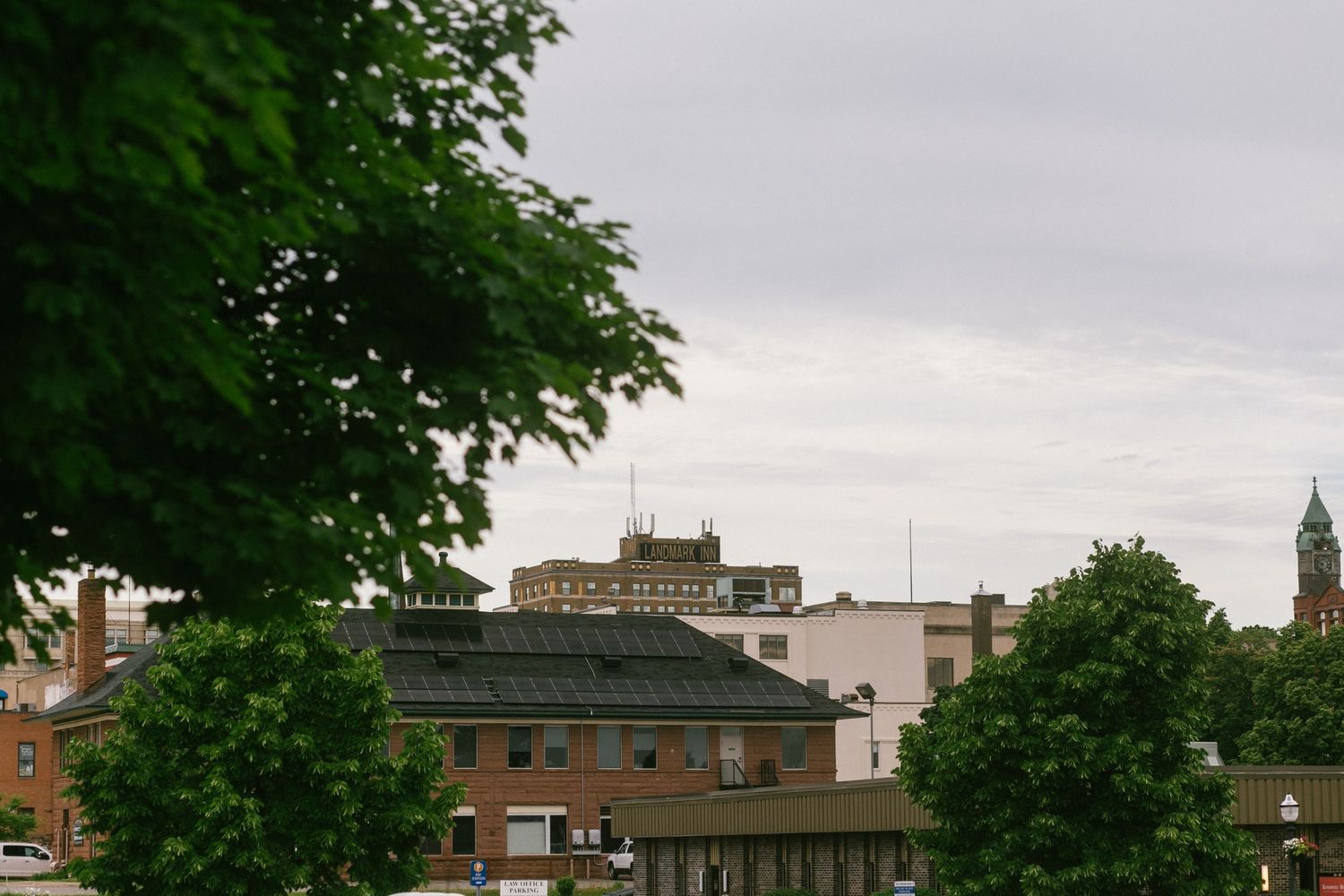 Urban cityscape view with trees framing buildings and rooftops against an overcast sky.