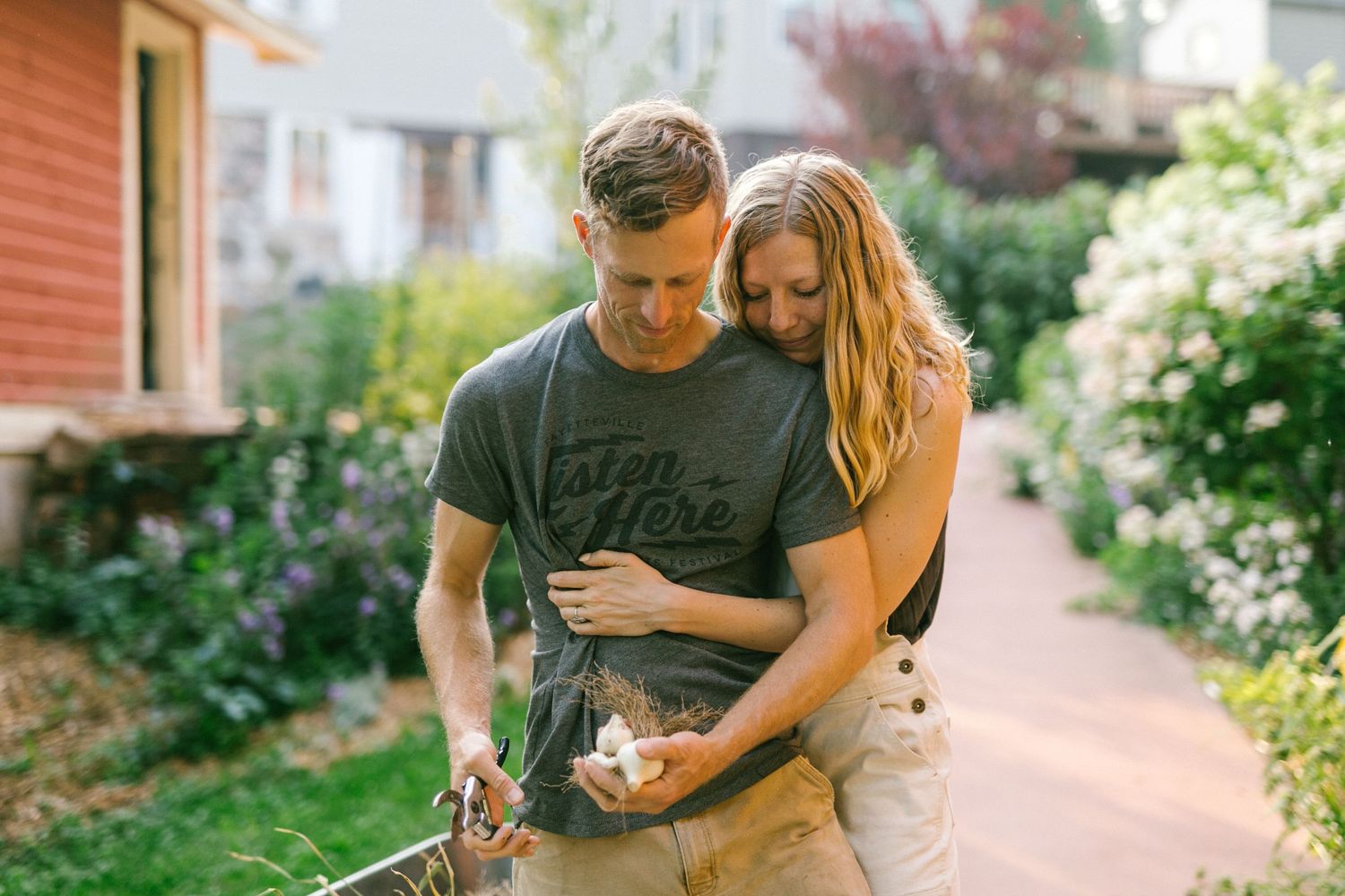 Couple embracing while cooking outdoors in a blooming garden pathway.