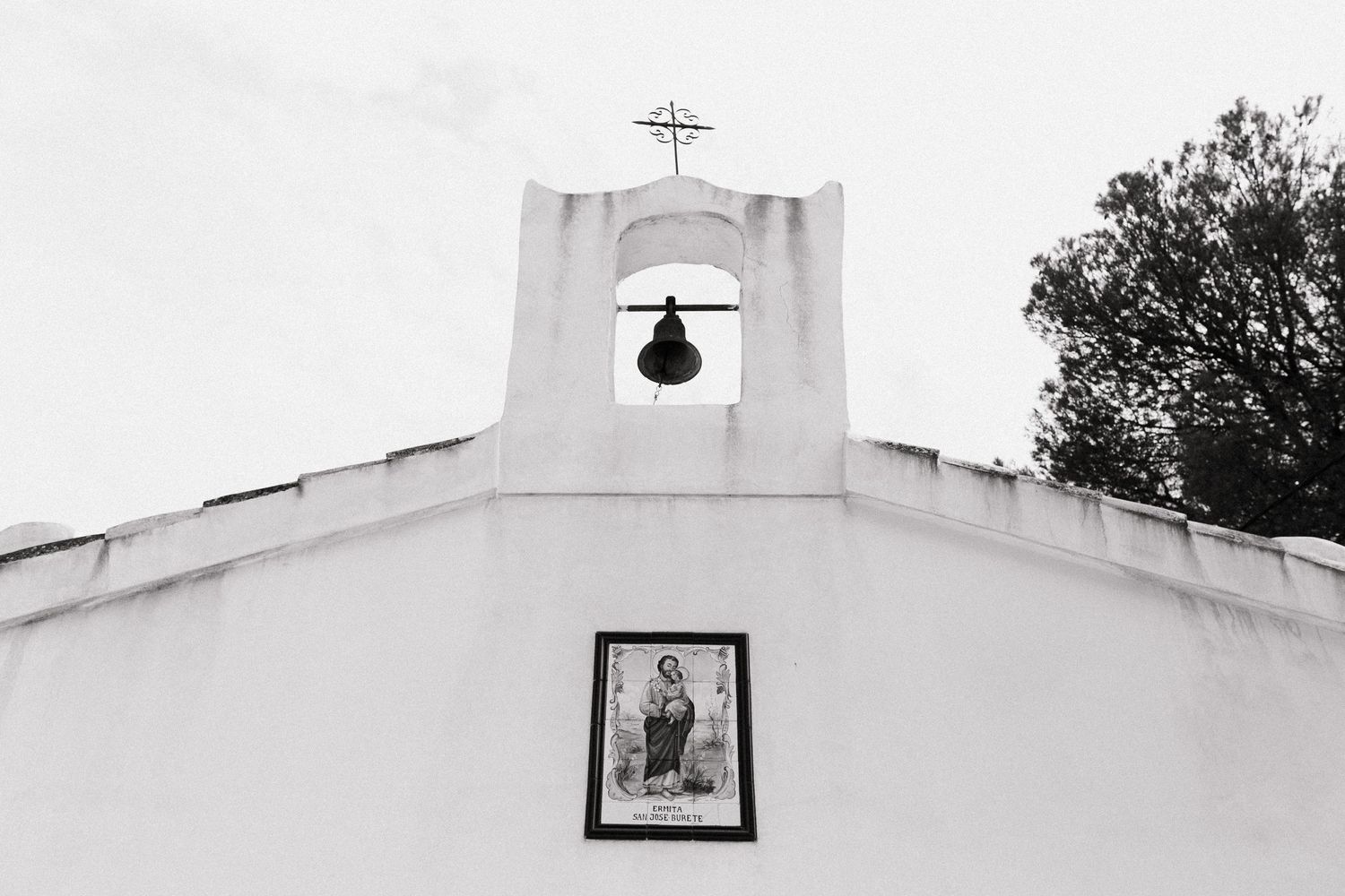 Black and white view of a white stucco church bell tower with a framed religious image below it.
