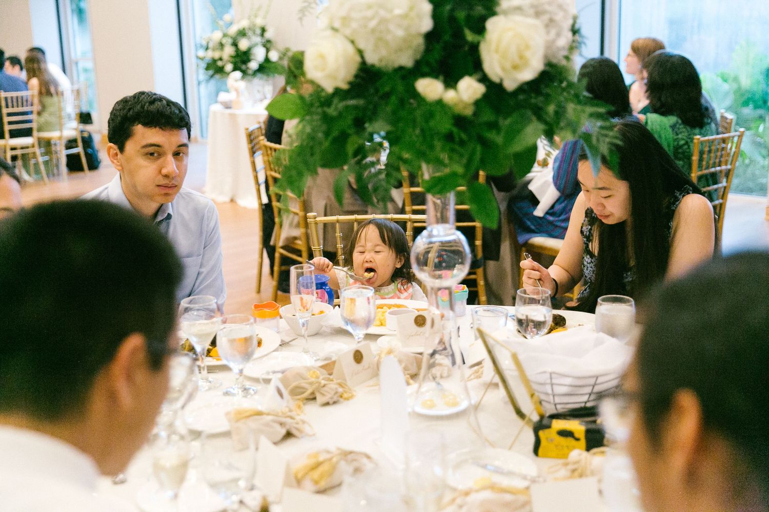 Child playing with bubble at elegant wedding reception table with floral centerpiece and guests.