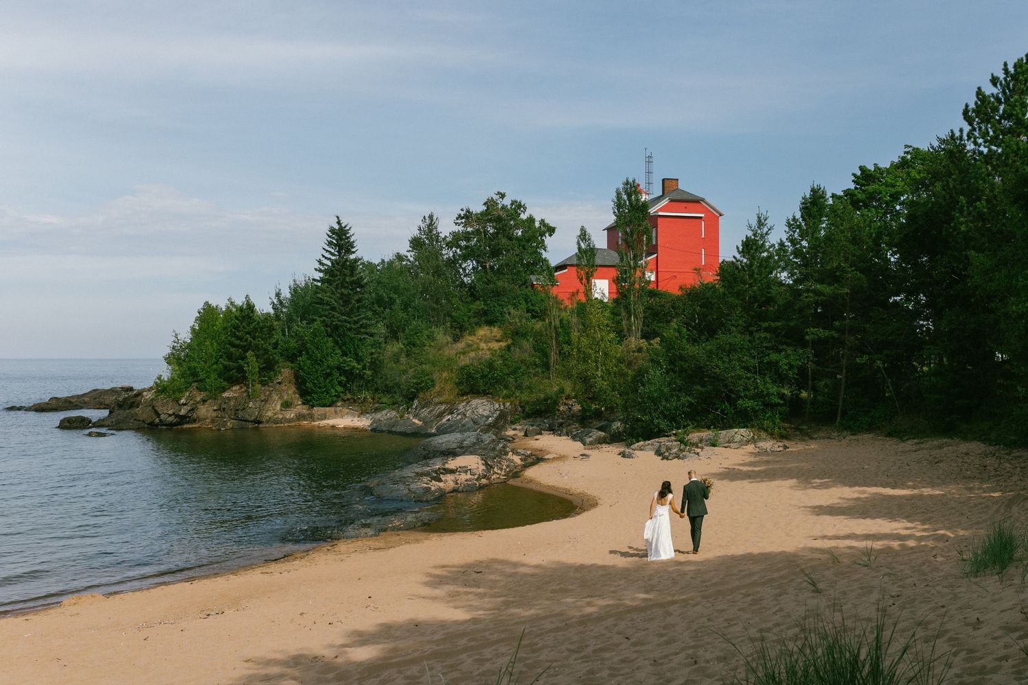 Scenic coastal landscape with a red lighthouse perched on rocky shores and a sandy beach path.