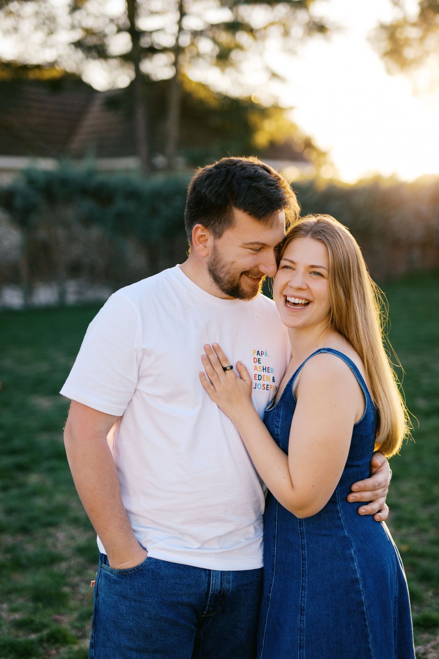 Joyful couple laughing and embracing in a sunlit outdoor setting at golden hour.