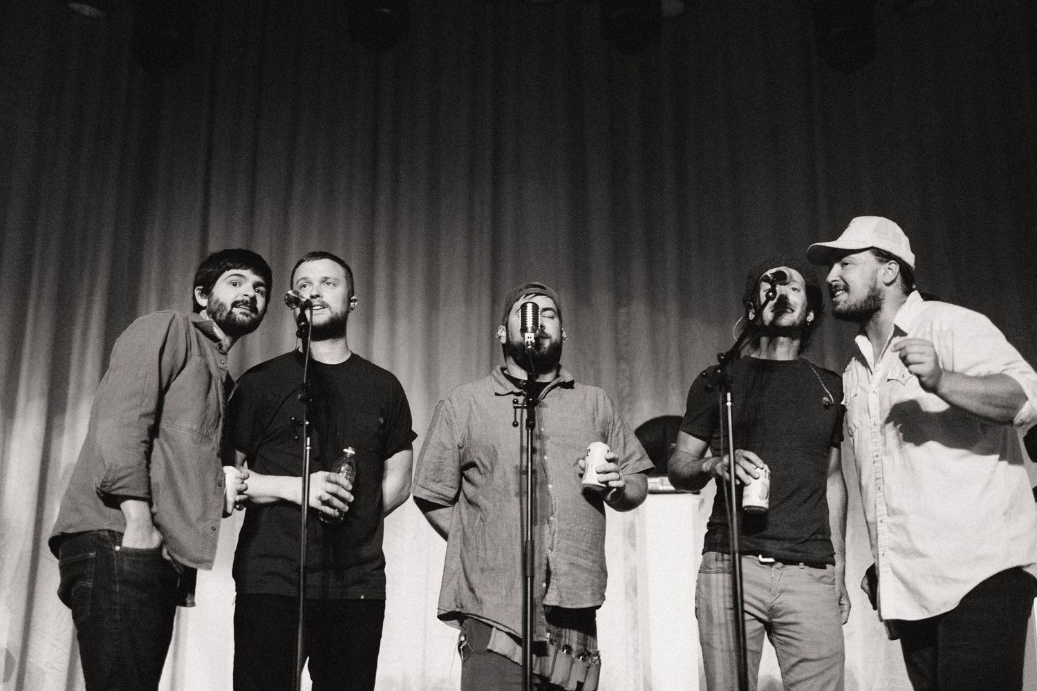 Black and white photo of performers singing together on stage with microphones.