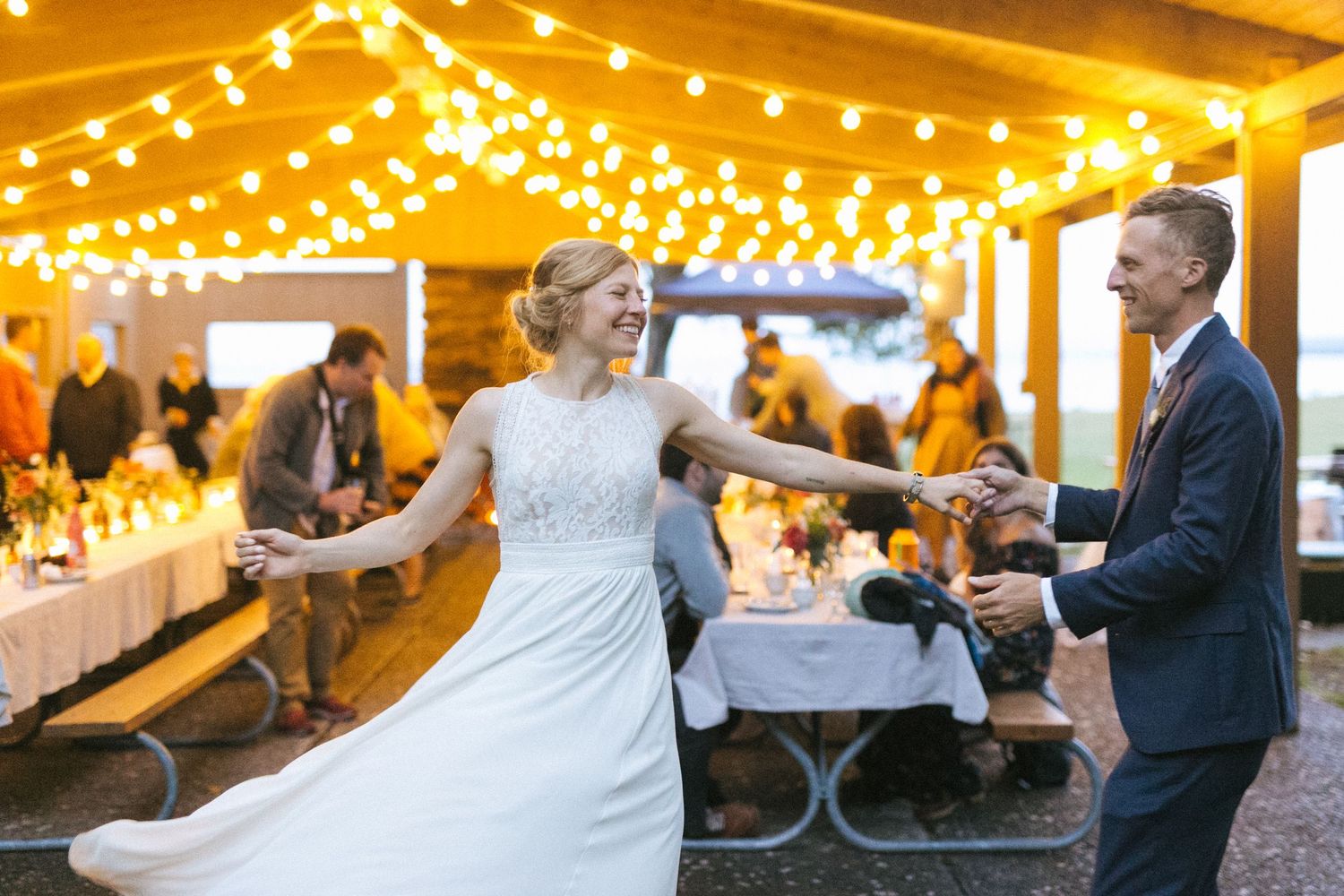 Couple dancing at outdoor wedding reception under glowing string lights.
