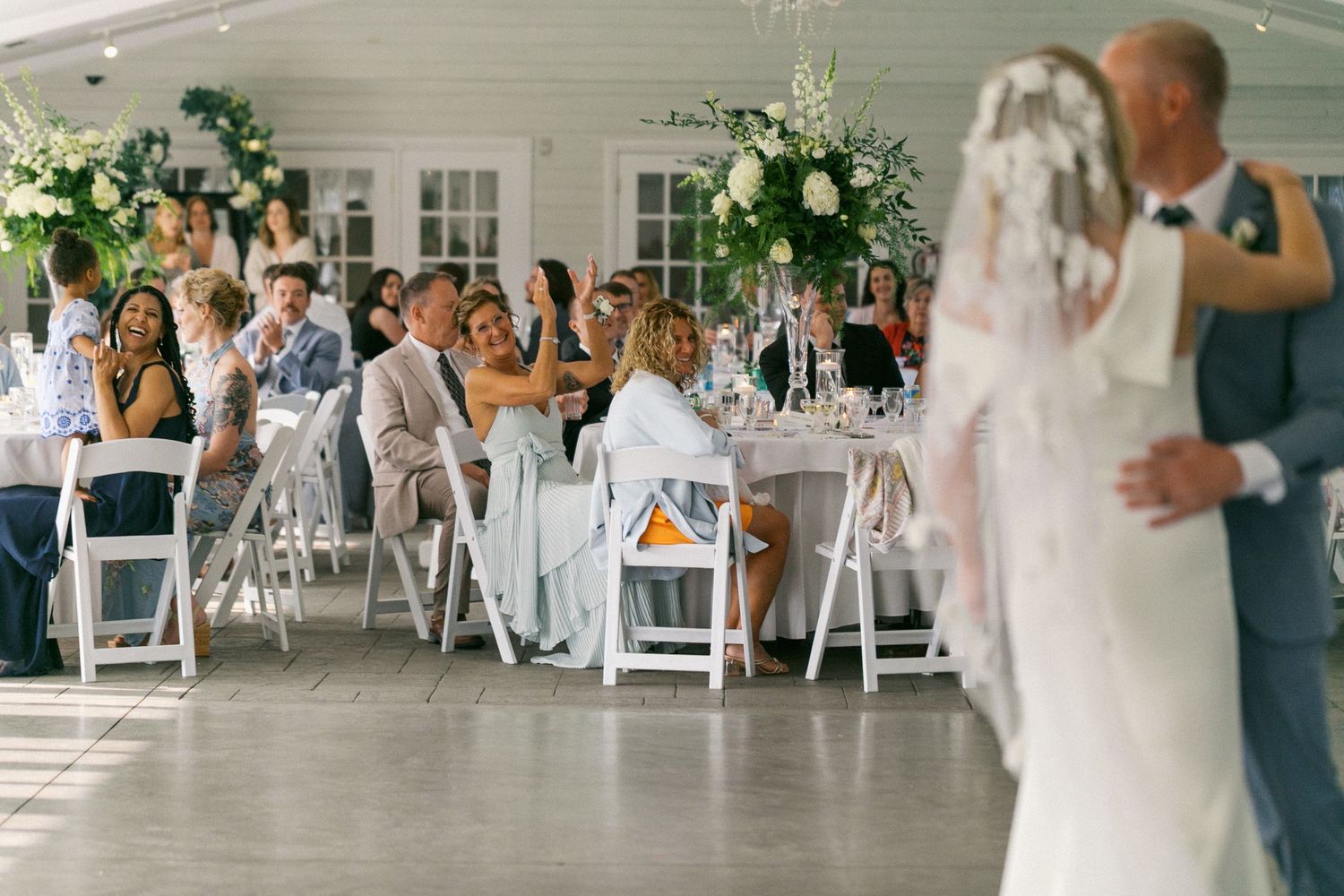 Wedding guests seated in white chairs at an elegant indoor ceremony with floral arrangements.