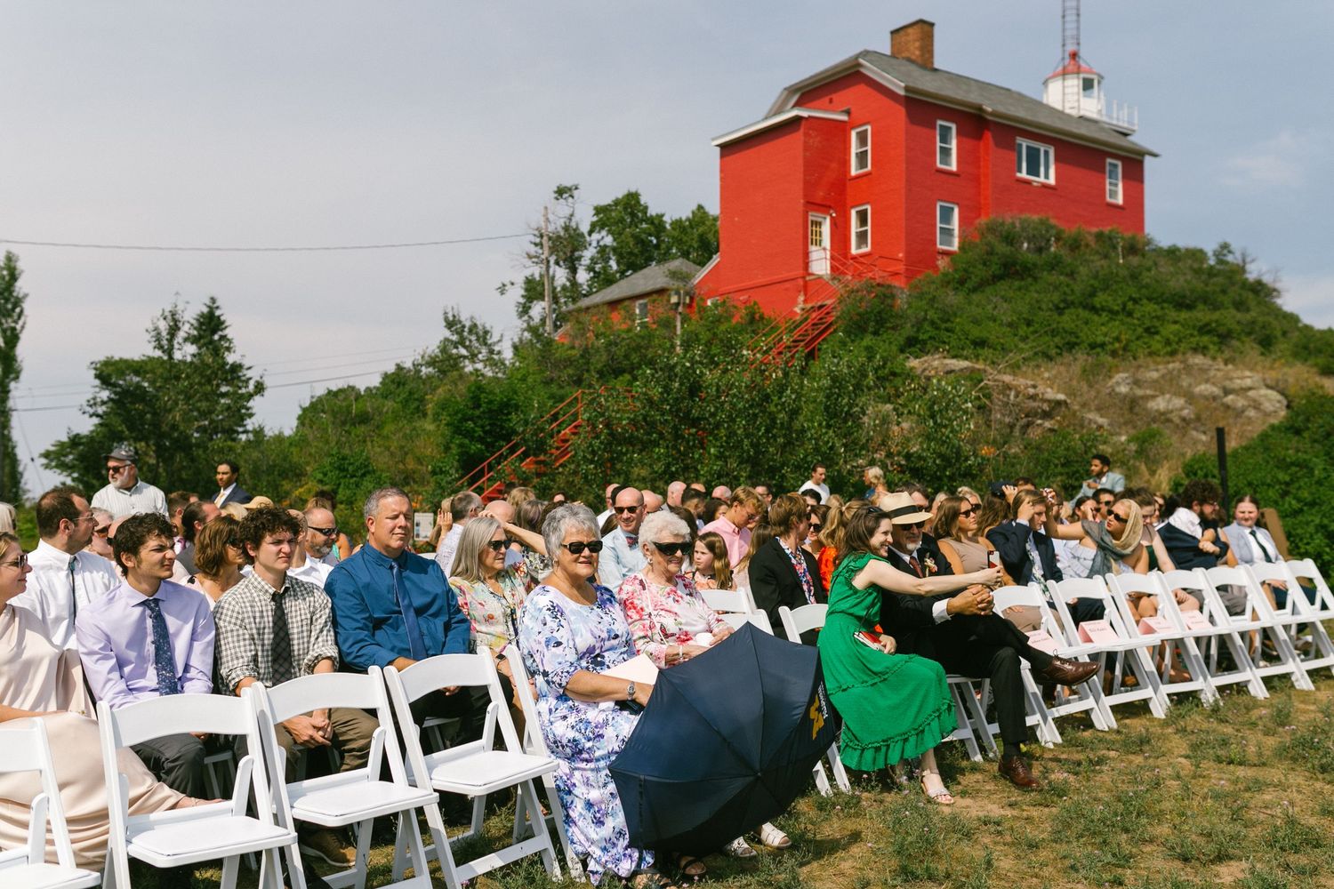 Red lighthouse building sits atop a hill with wedding ceremony chairs in the foreground.