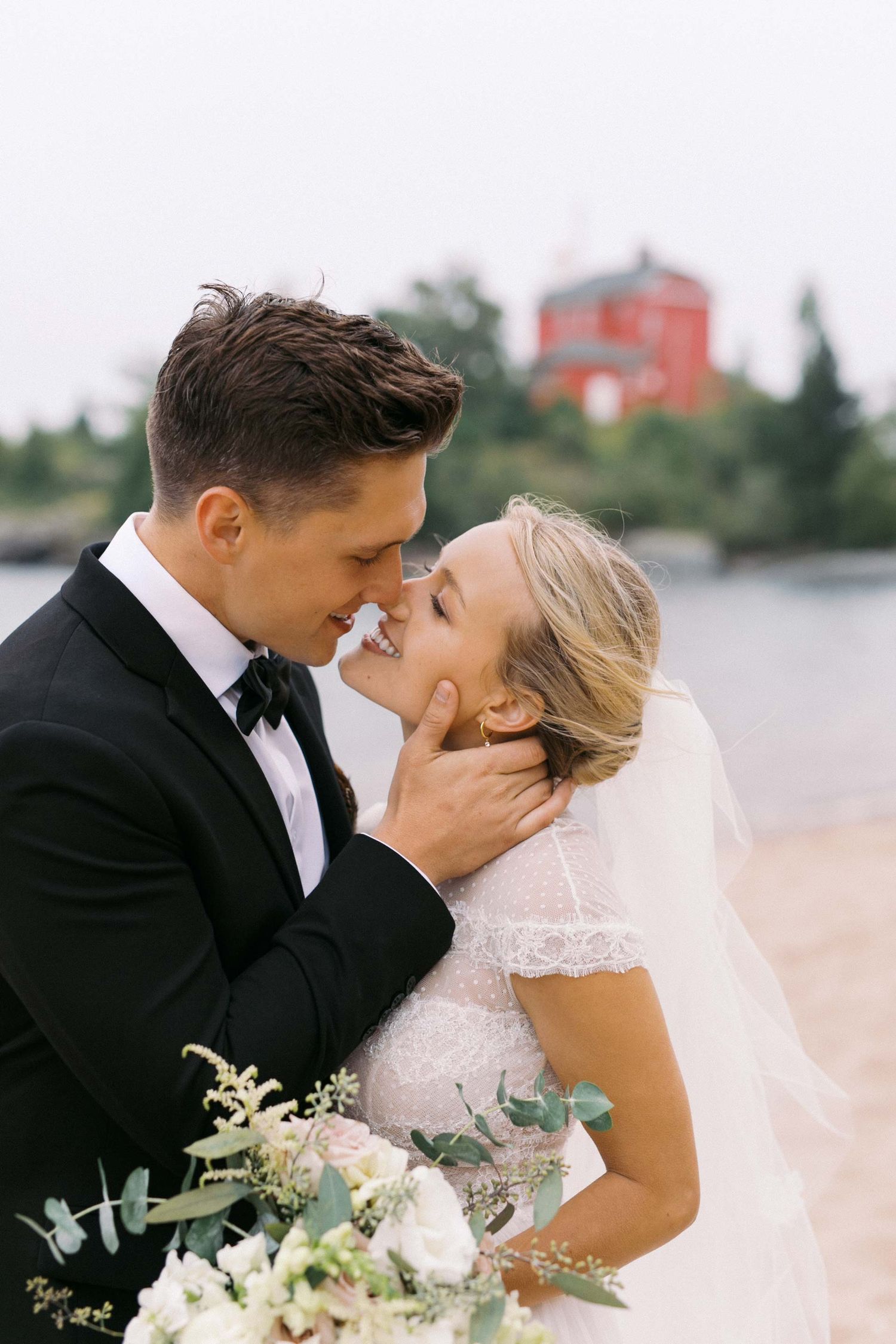 A romantic wedding couple shares an intimate kiss while holding a delicate bouquet of white flowers and greenery.