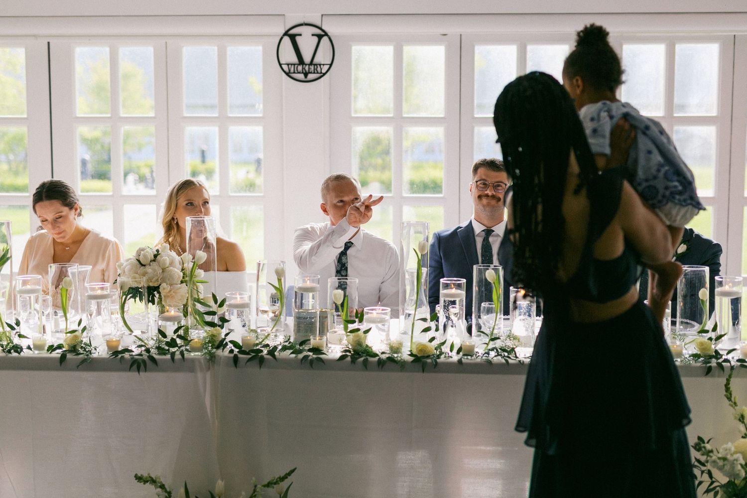 Elegant wedding reception table settings in bright white room with large windows.