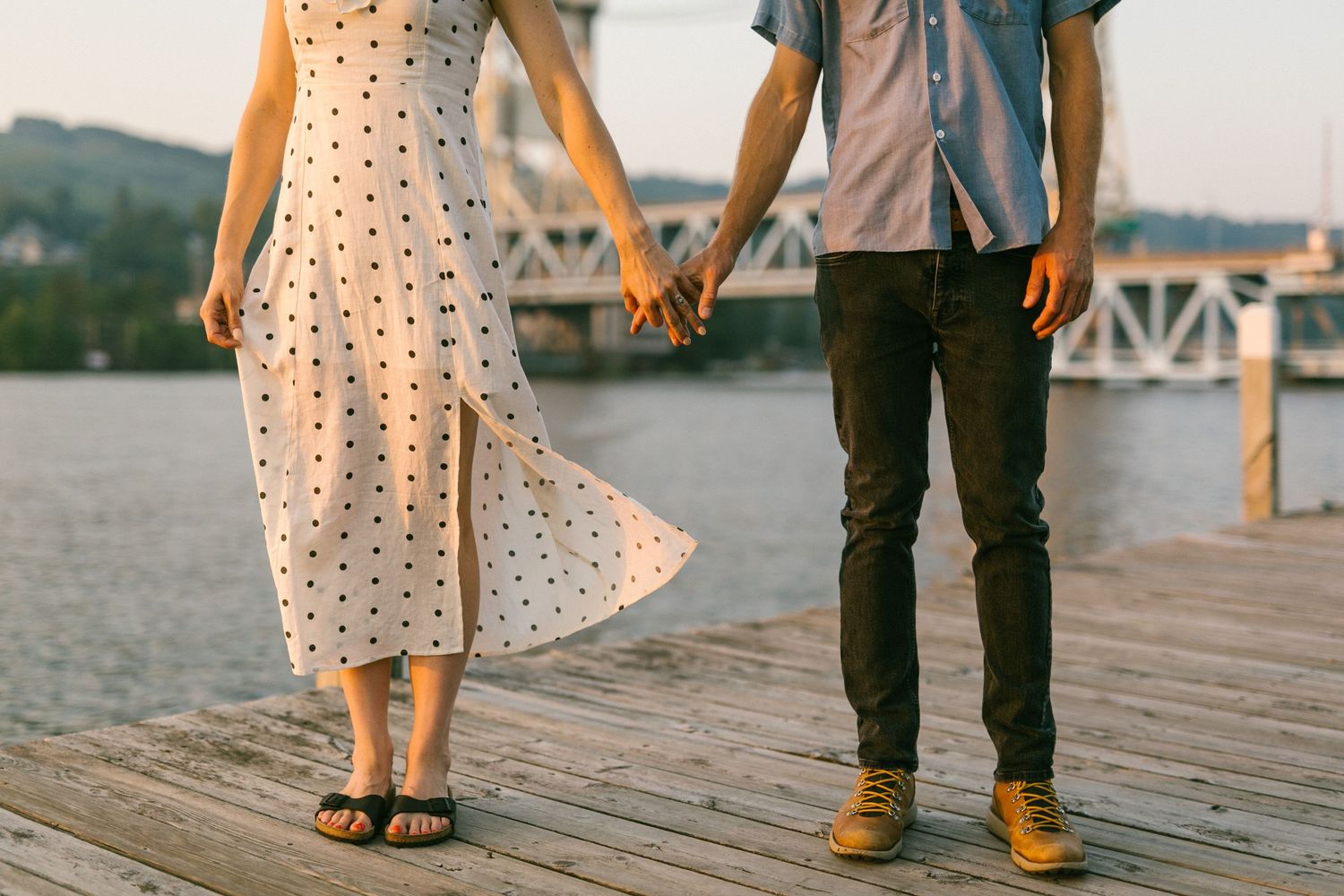 Close-up of polka dot dress and casual attire as couple stands on wooden dock by the water.