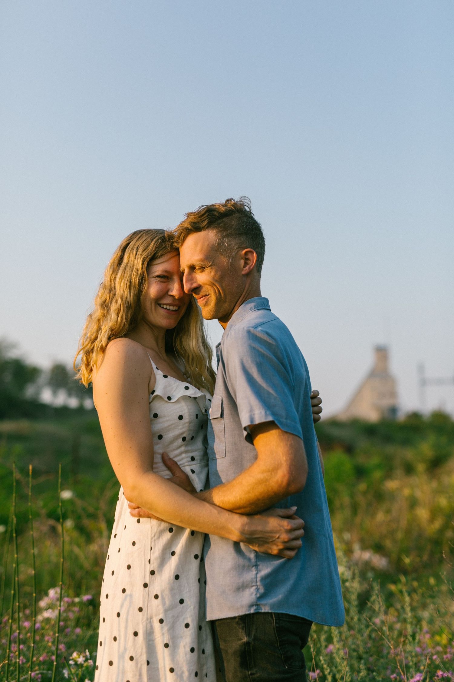 Intimate moment between a couple in casual summer attire standing in a wildflower field.