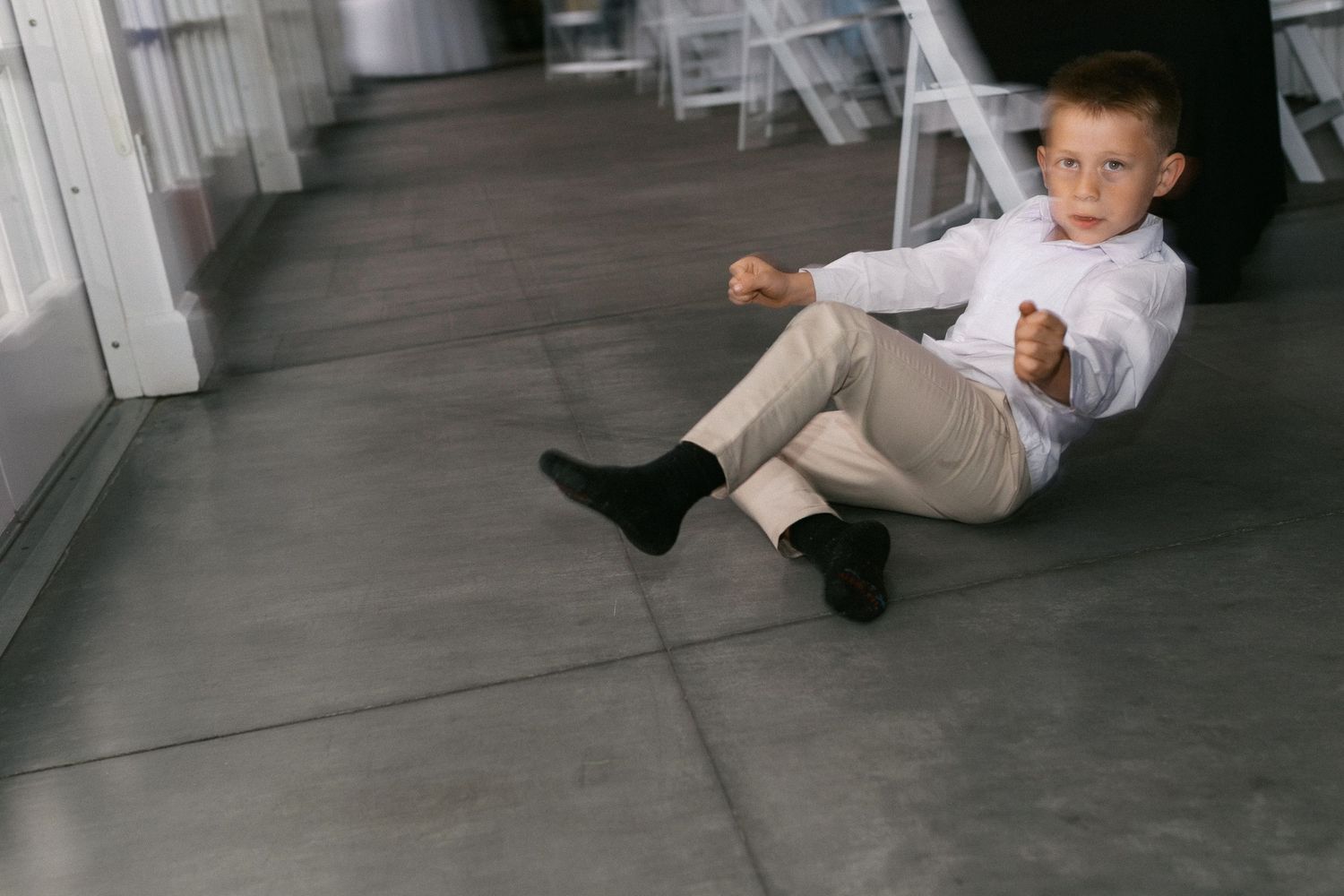 Playful children in formal attire sliding across a polished floor at a wedding reception.