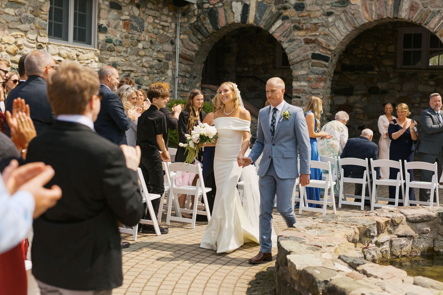 Wedding guests gathering outside a rustic stone building for an outdoor ceremony.