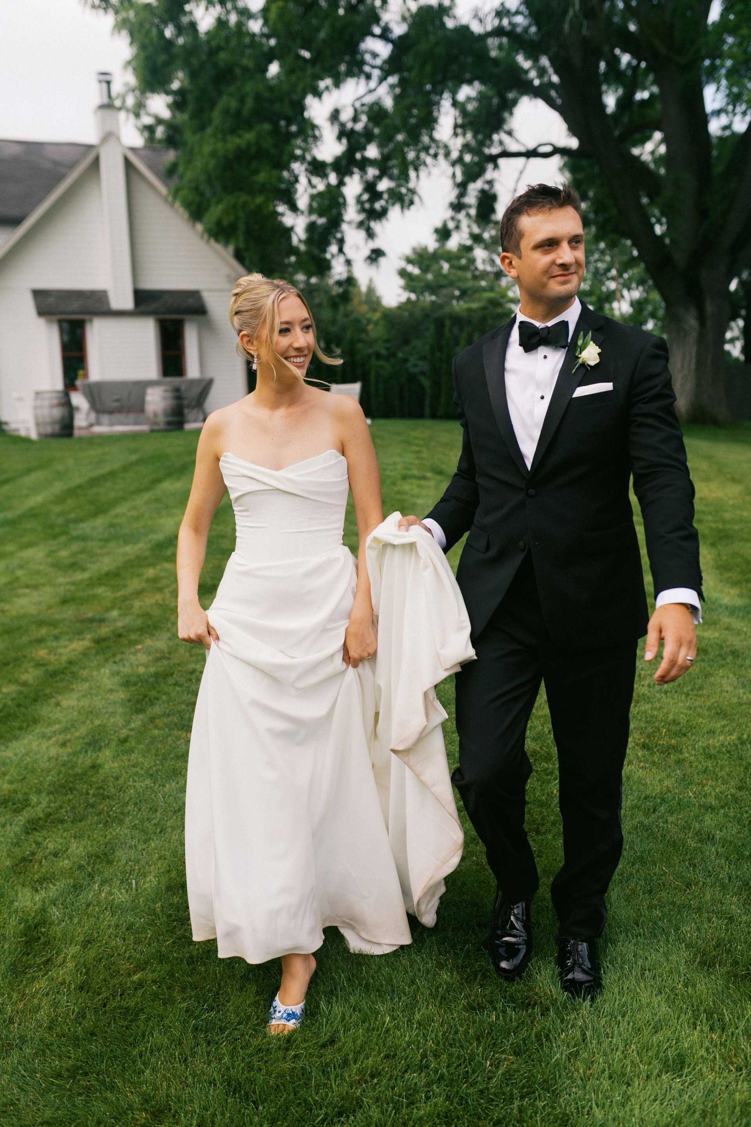 A couple in wedding attire walks together on a lush green lawn showing their blue shoes during an outdoor celebration.