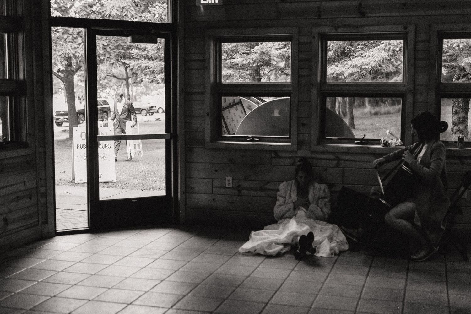 A white dog rests on a tiled floor near an open door in a rustic black and white composition.