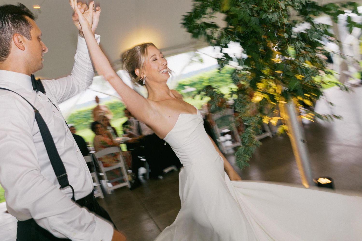A joyful couple dances together at their wedding reception, with the bride wearing a strapless white gown.