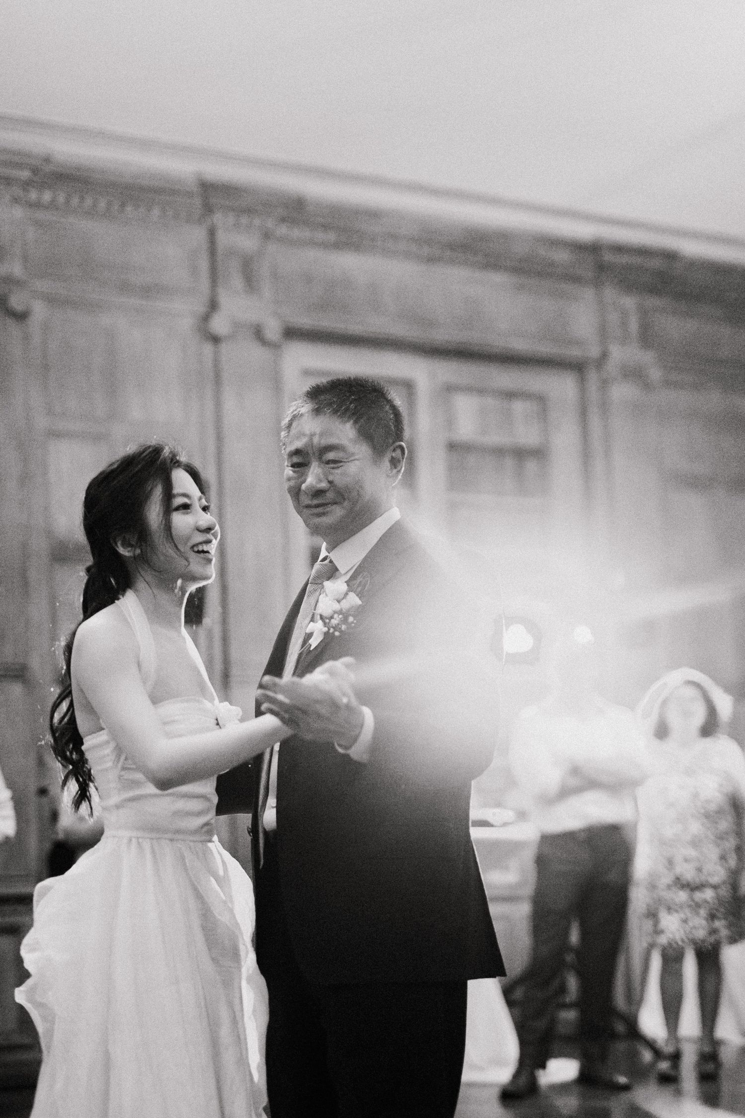 Bride and father share an emotional first dance at wedding reception in black and white photo.