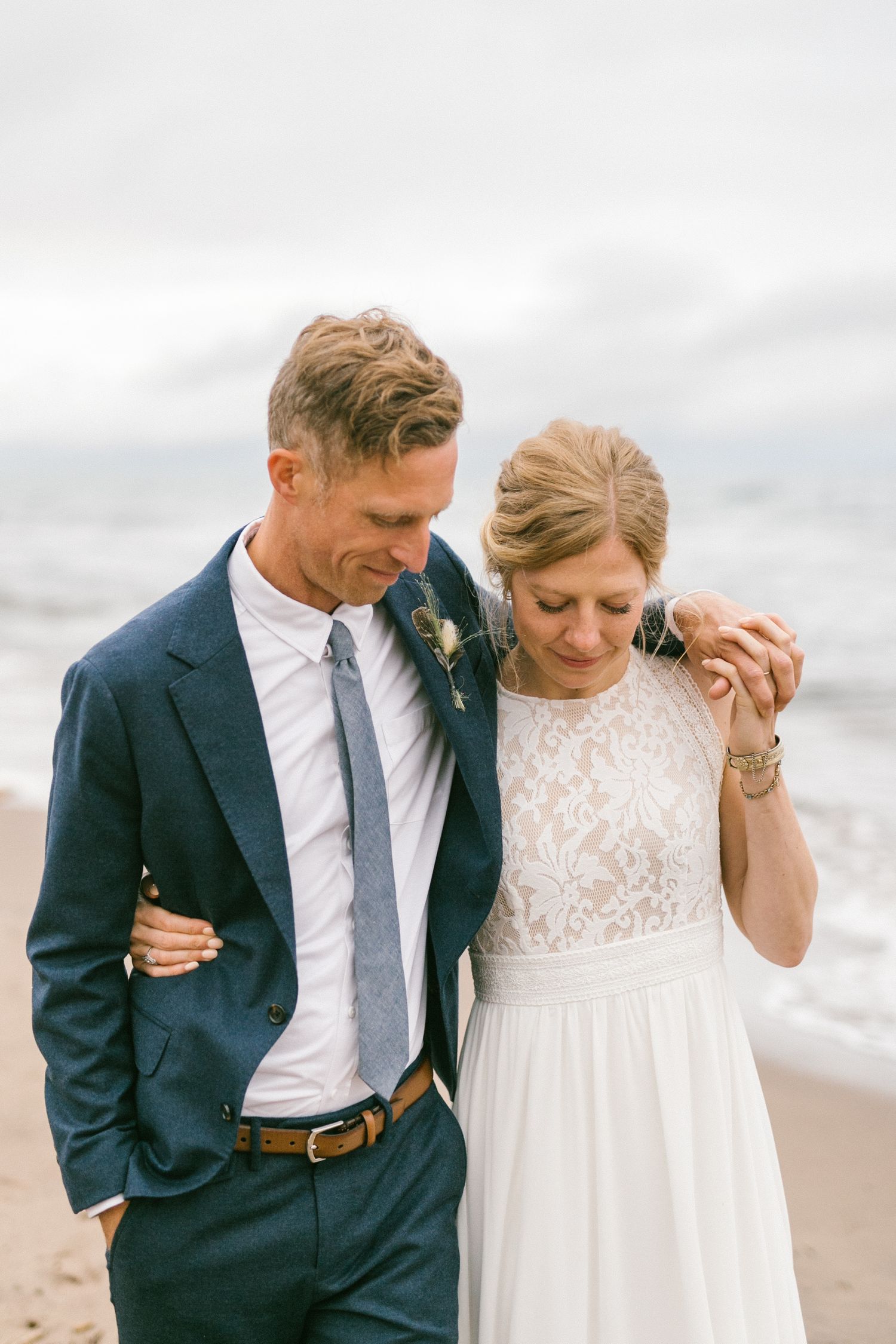 An intimate wedding portrait on the beach with overcast skies and gentle waves.