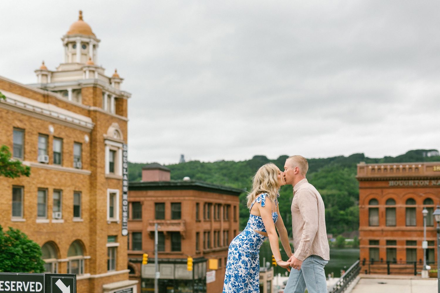 A couple shares a romantic moment in front of historic brick buildings in a small town setting.