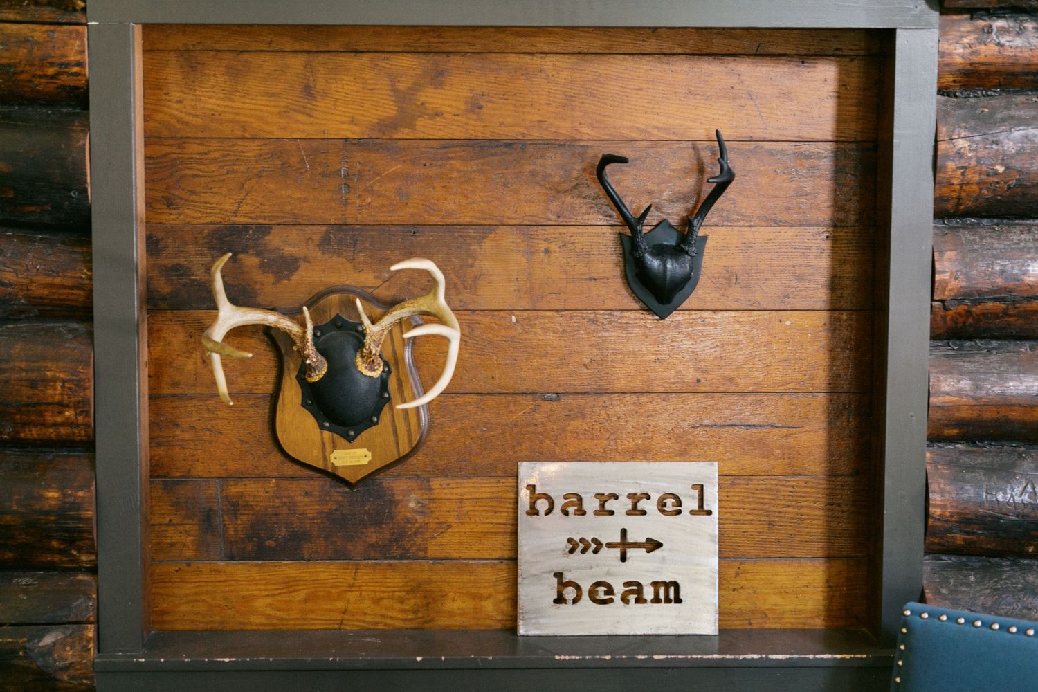 Rustic wooden wall with mounted deer antlers and a 'barrel beam' sign in a log cabin setting.