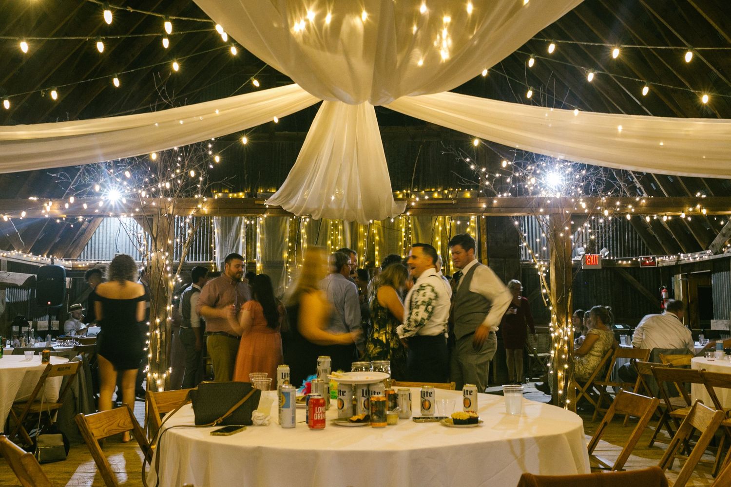 String lights and white fabric drape elegantly over an outdoor evening wedding reception space creating a romantic ambiance.