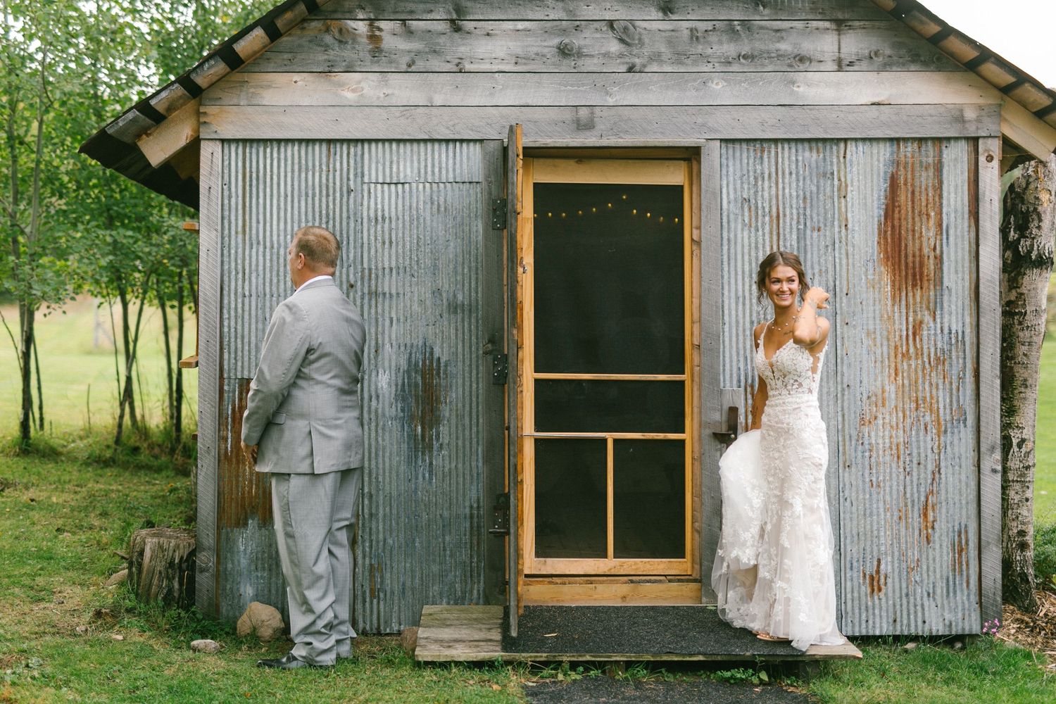 A father and daughter emotionally wait on opposite sides of a rustic wooden screen door for their first look on the brides wedding day.