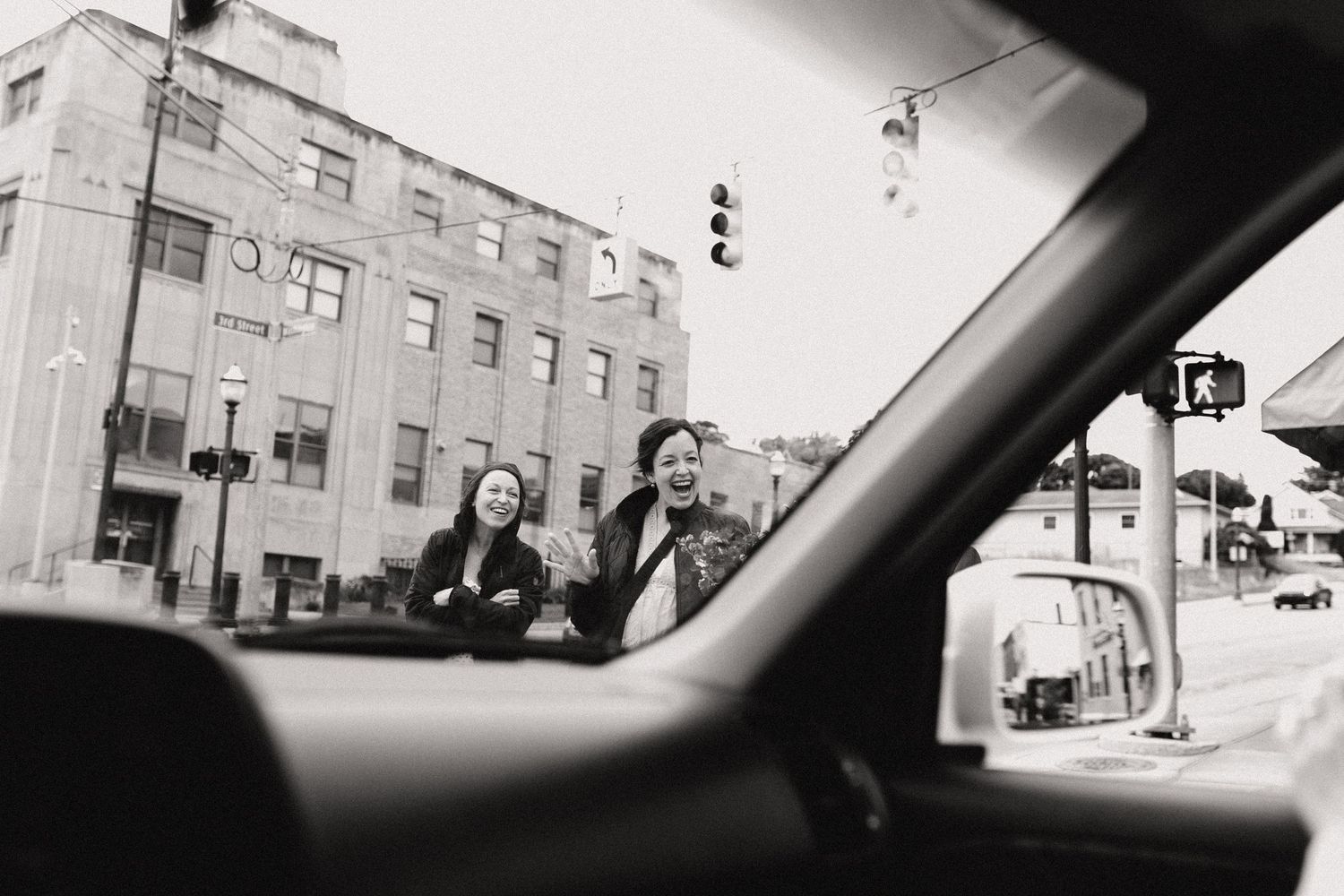 Black and white street scene photographed through a car window showing pedestrians crossing at an intersection.