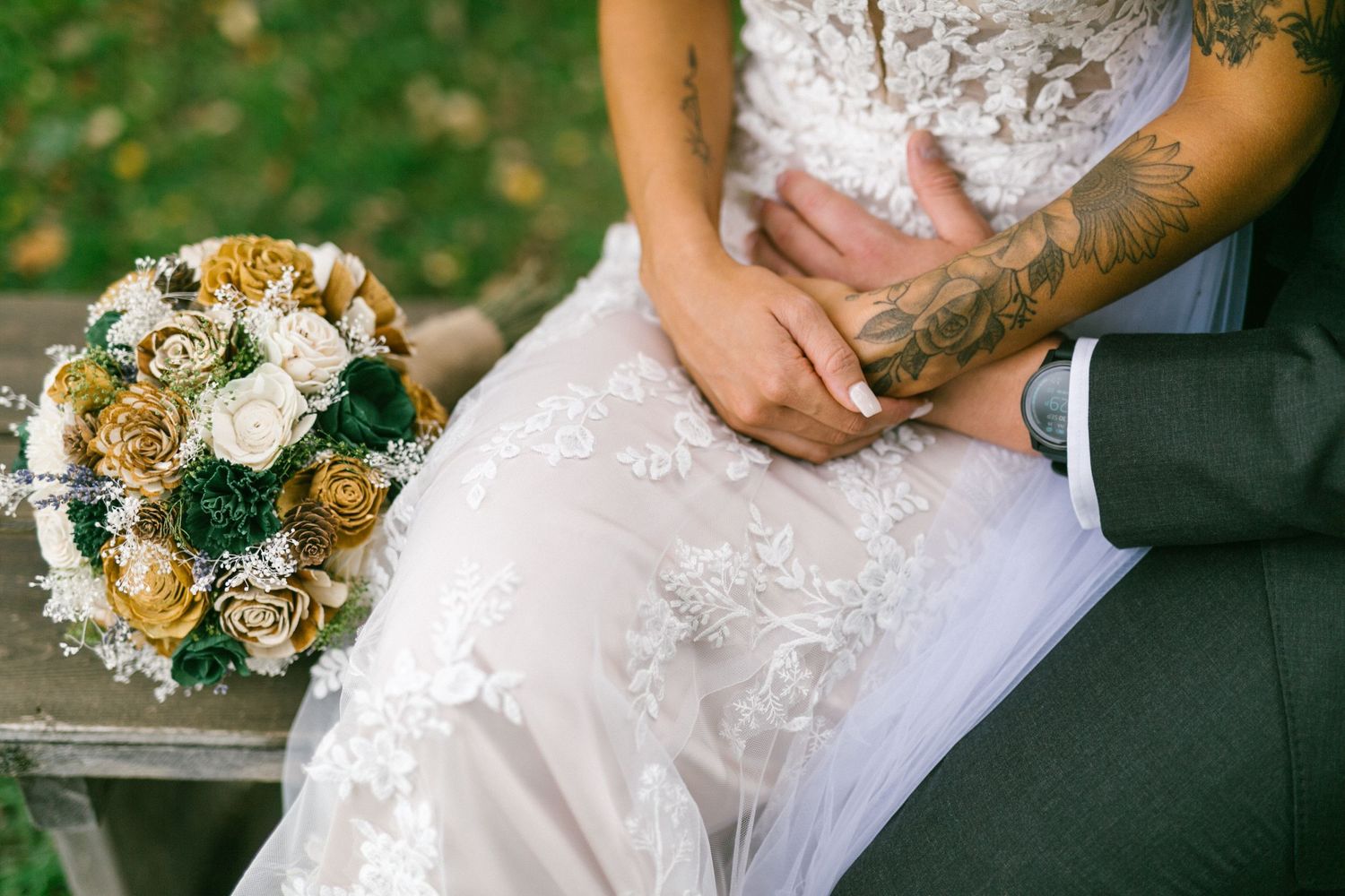 Wedding bouquet with white and yellow flowers rests beside newlyweds sitting together on a bench.