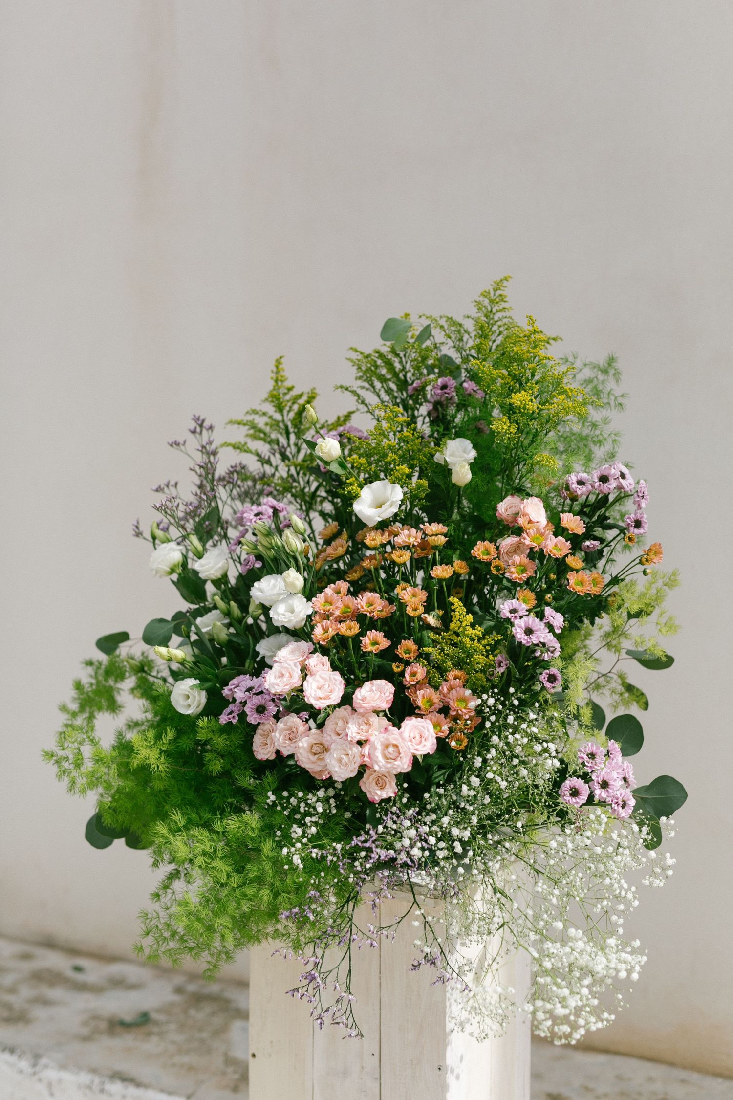 Beautiful rustic floral arrangement with pink roses, peach flowers, and delicate white baby's breath in a light-colored container.