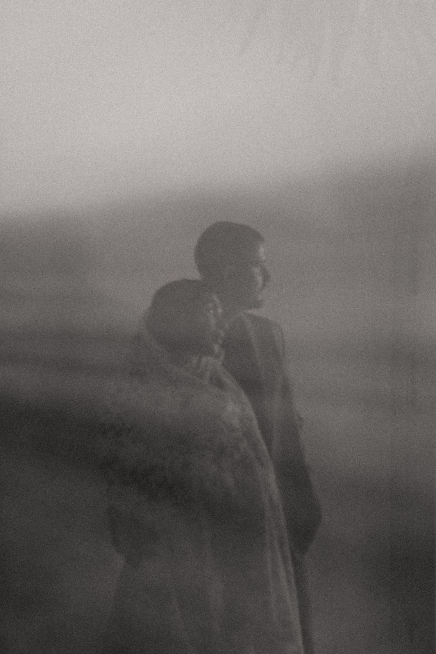 Black and white double exposure photo of a couple embracing in misty fog, creating a dreamy romantic silhouette.