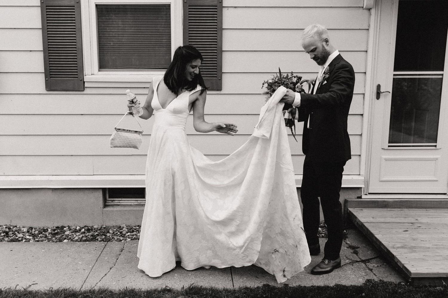 Black and white photo of wedding dress preparations against white house siding.